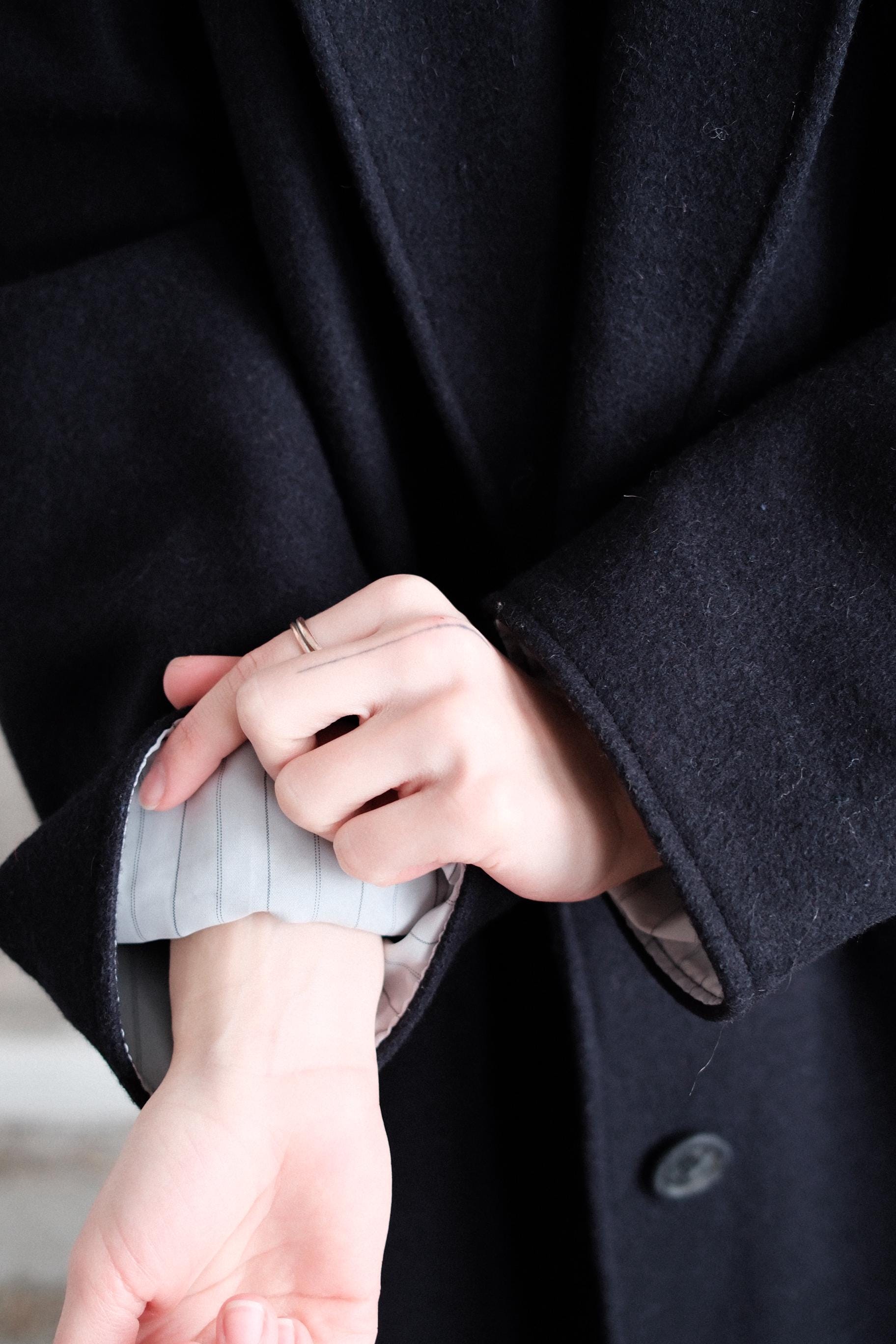 A close-up view of a person's hand wearing a ring and holding a sleeve of a black coat.