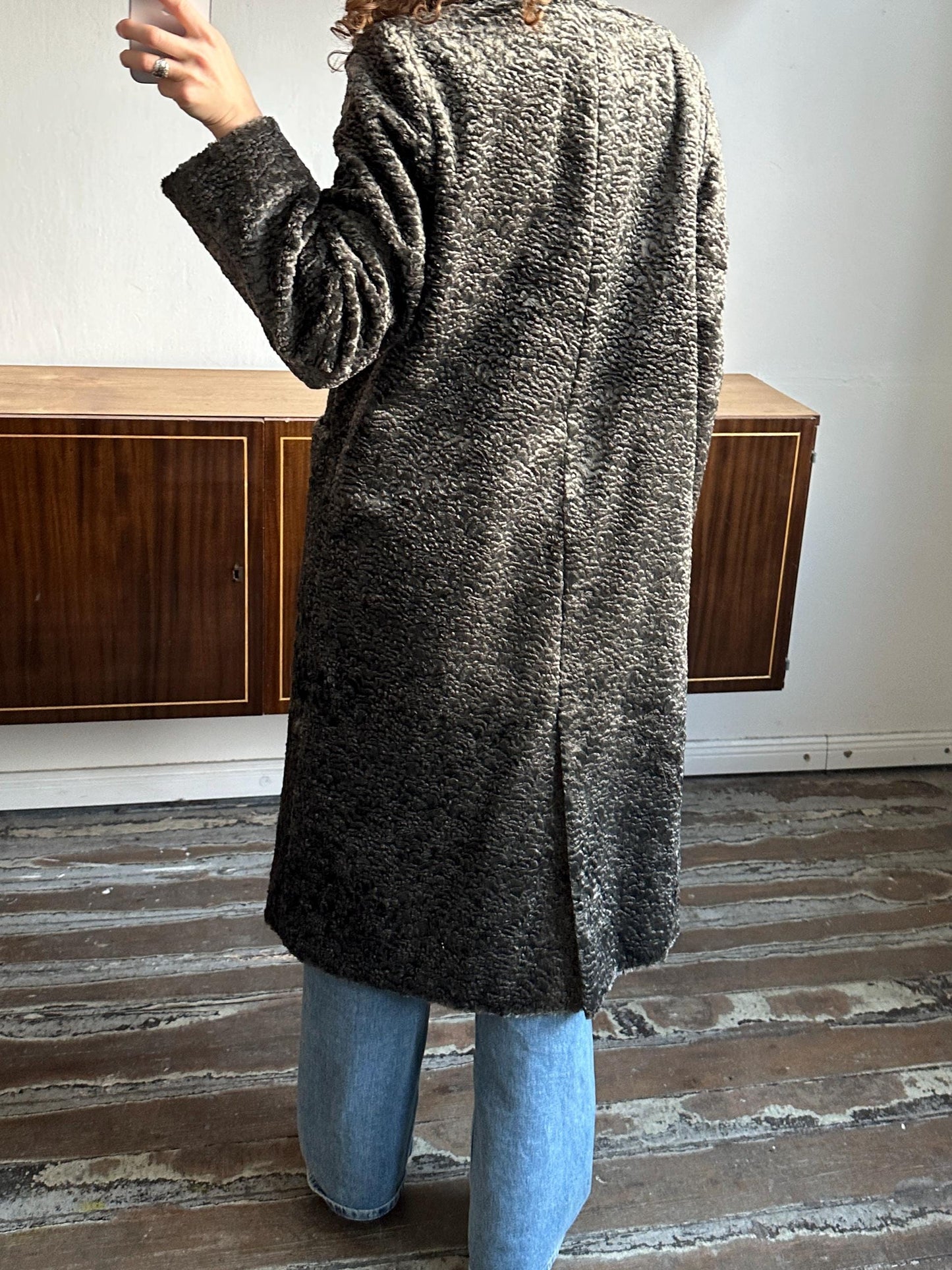 a person wearing a gray coat standing in a room with a wooden floor.