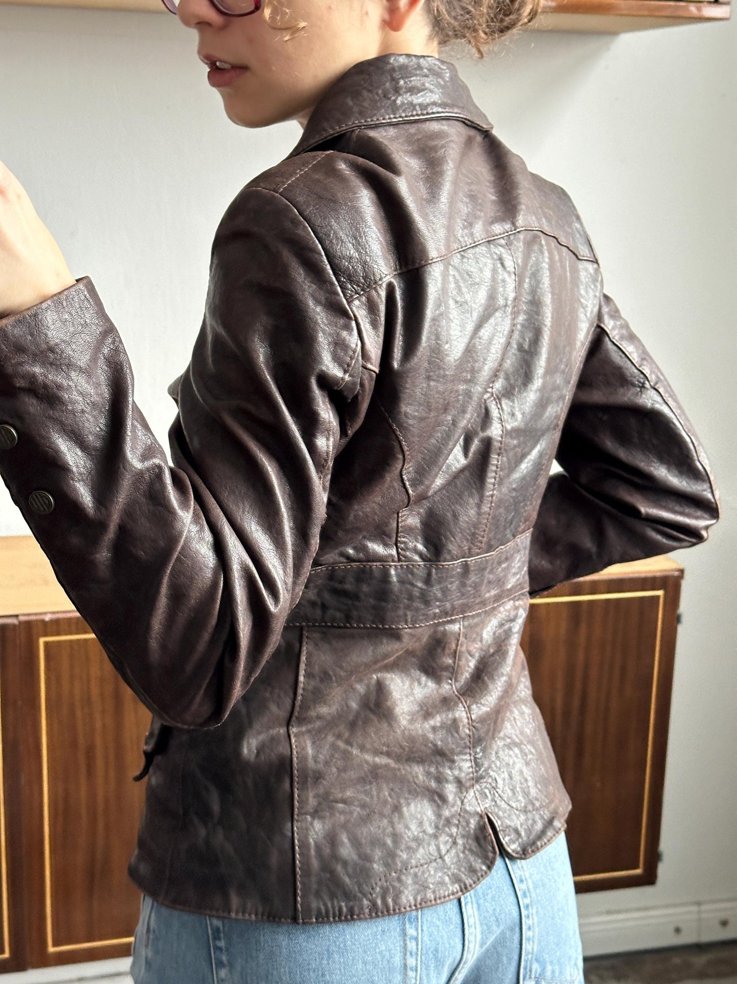 A person wearing a brown leather jacket is leaning back in a relaxed manner, with their head tilted downwards.