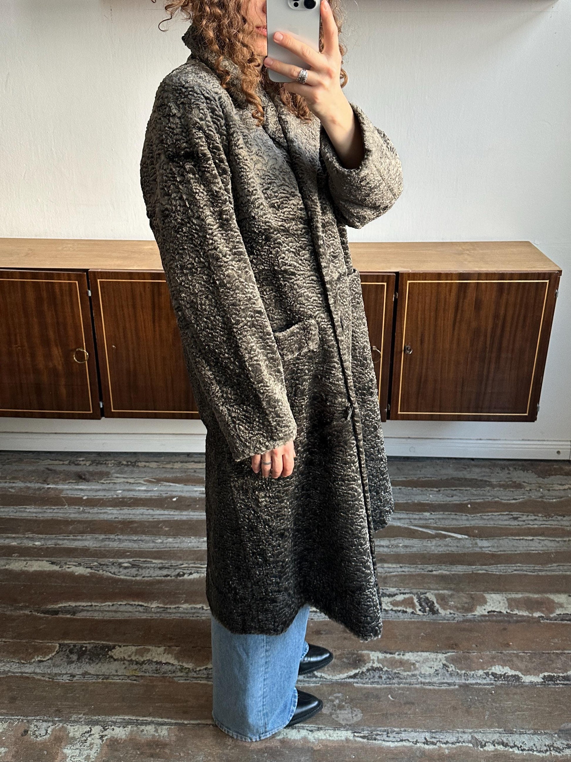 A person is taking a selfie with a smartphone, standing in front of a wooden cabinet.