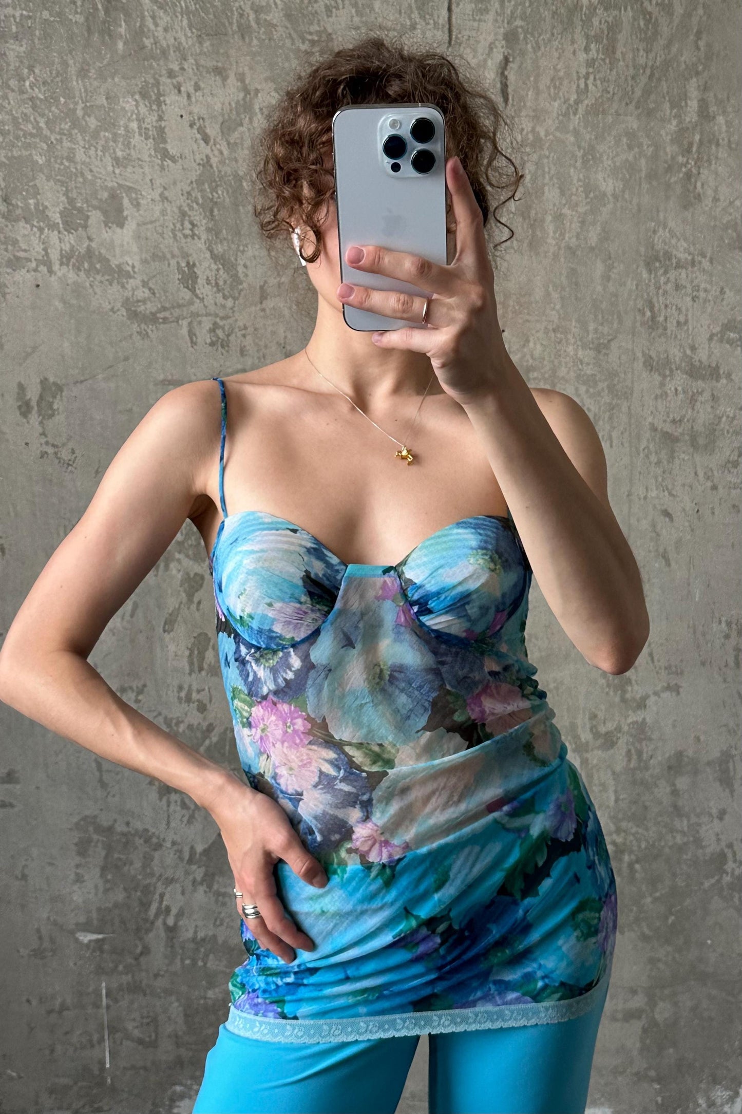 A woman is taking a selfie with her iPhone, wearing a blue floral dress.