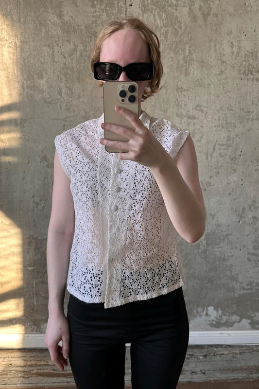 A woman wearing a white lace top and sunglasses is taking a selfie with her iPhone.