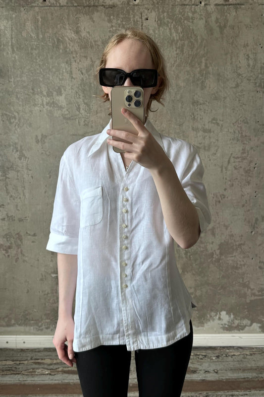 A person wearing a white shirt and sunglasses is taking a selfie with a smartphone.