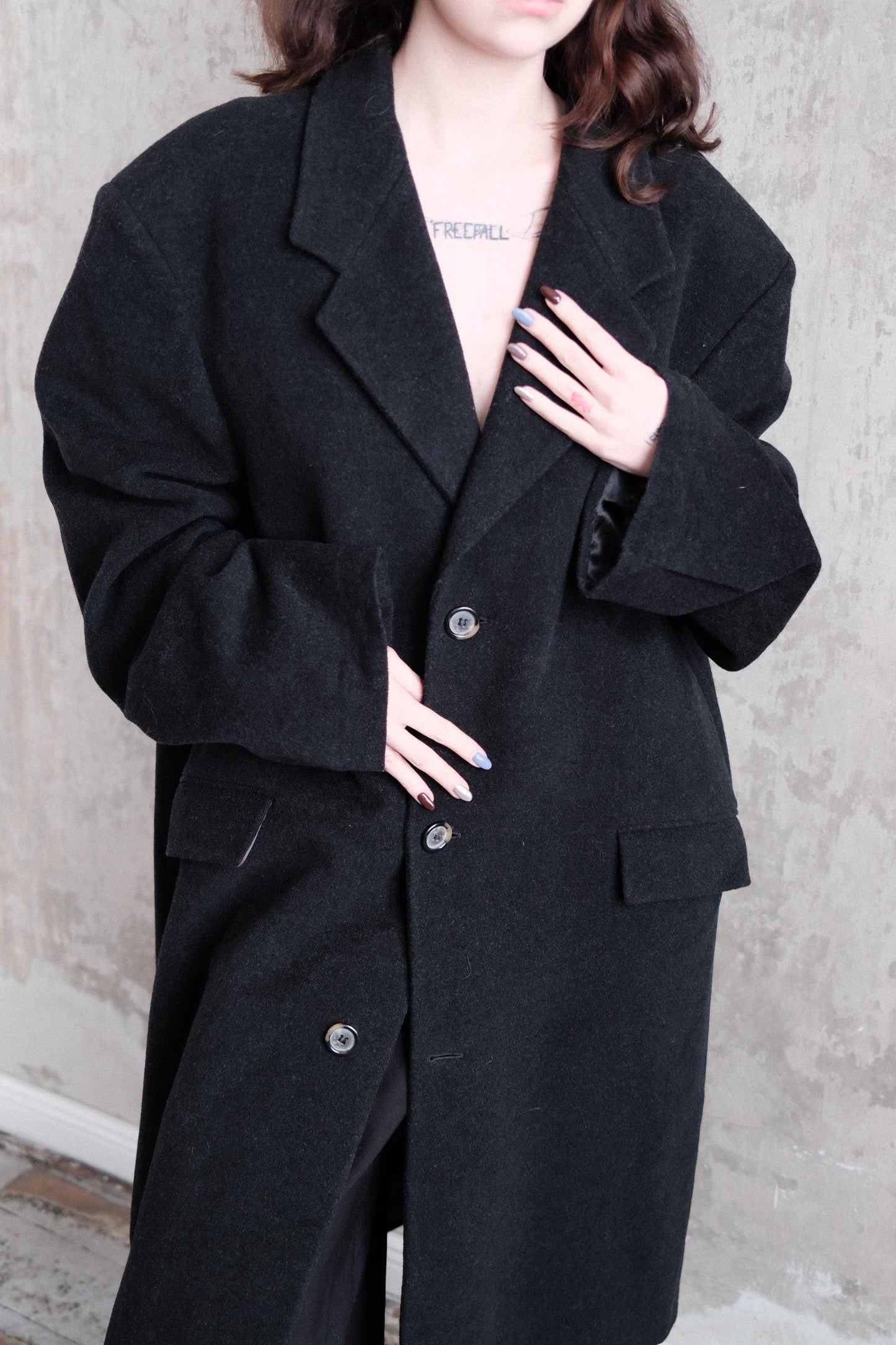 A person wearing a black coat is standing on a concrete floor.
