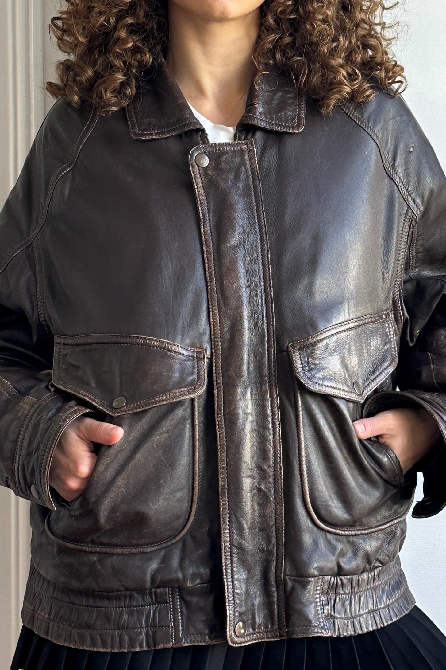 A close-up of a person wearing a brown leather jacket with a collar and two pockets.