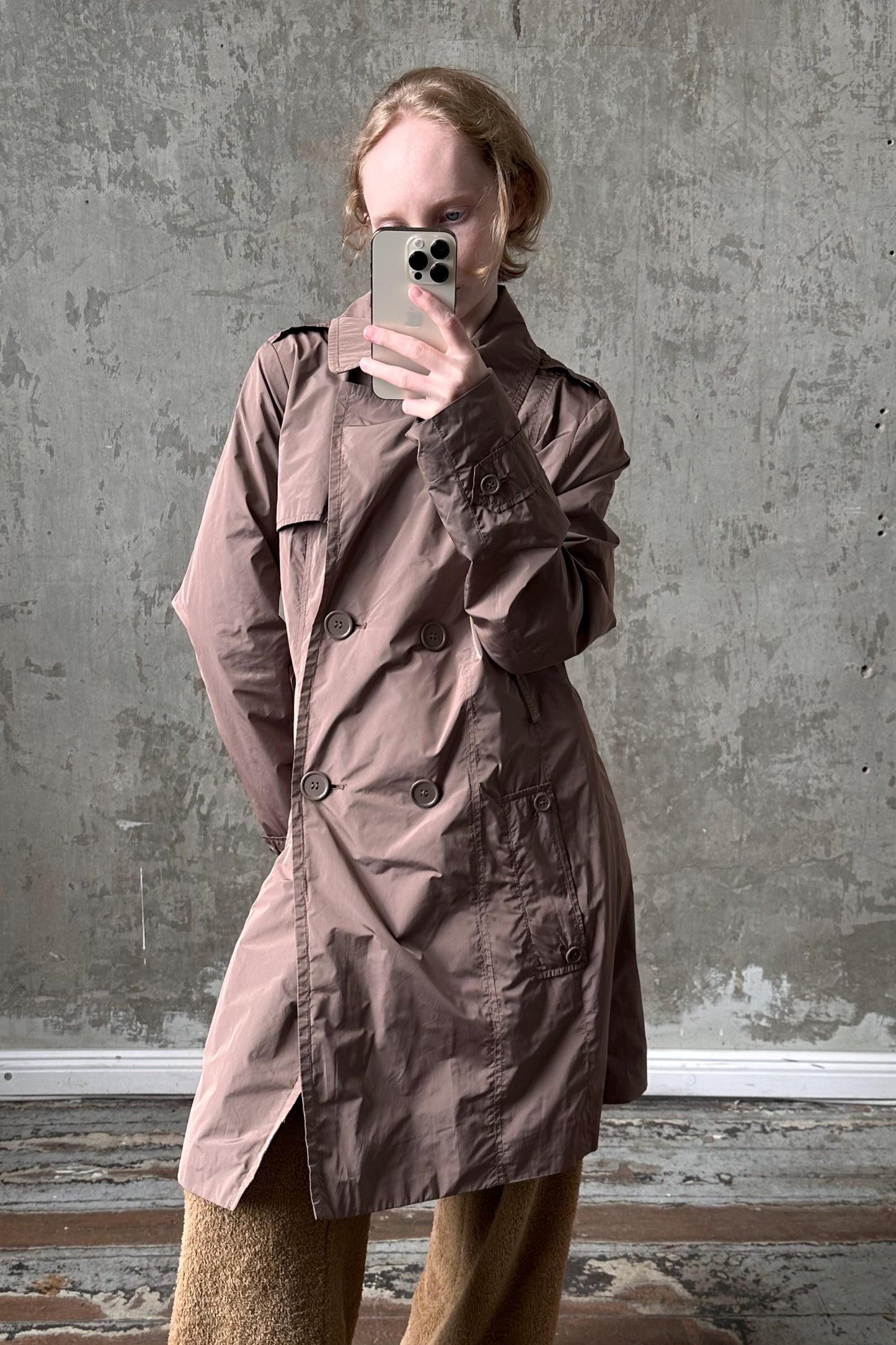 A person is taking a selfie with a smartphone, wearing a brown trench coat.