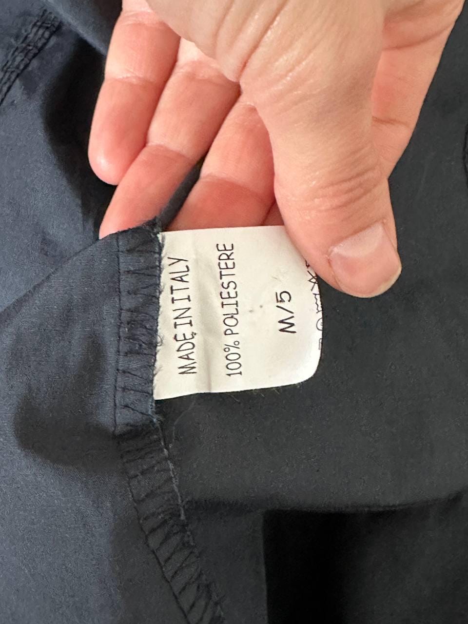 A hand is holding a label with text on it, which appears to be a label for a garment.