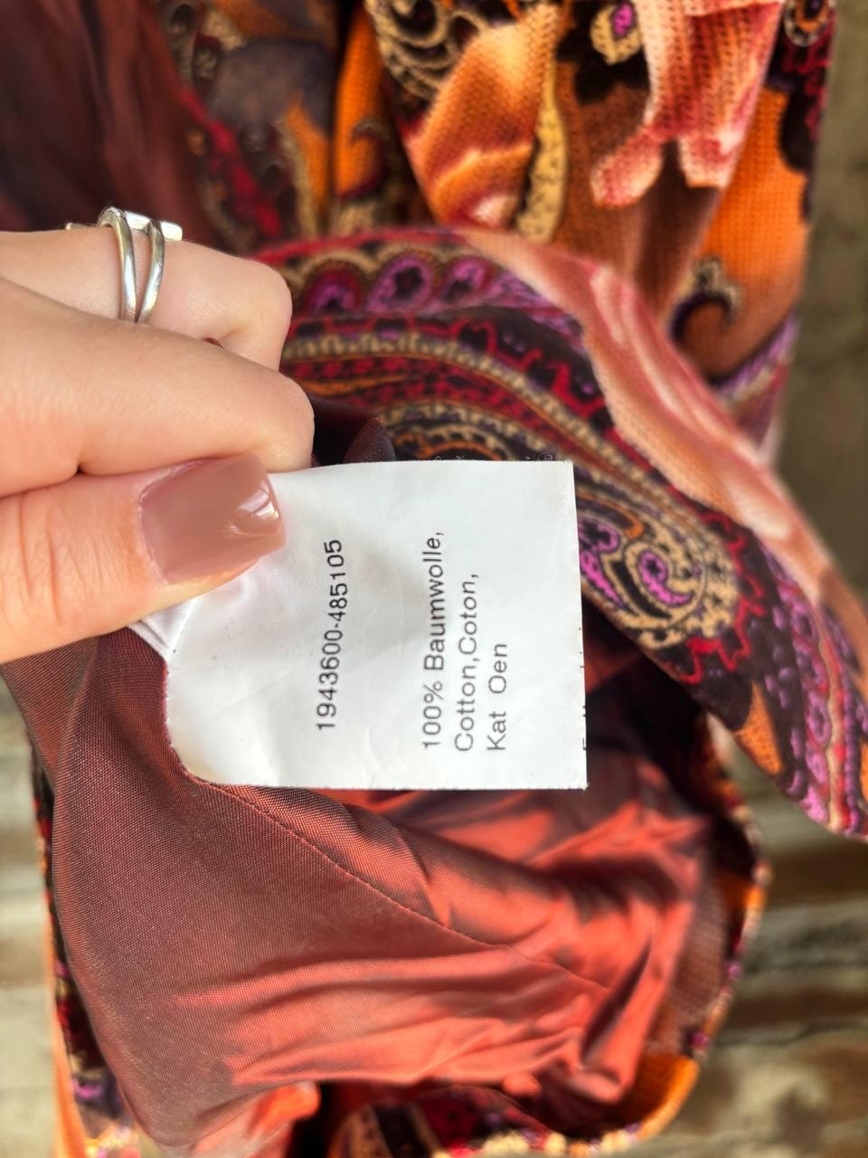 A hand holding a label with text on it, against a background of a colorful, patterned fabric.