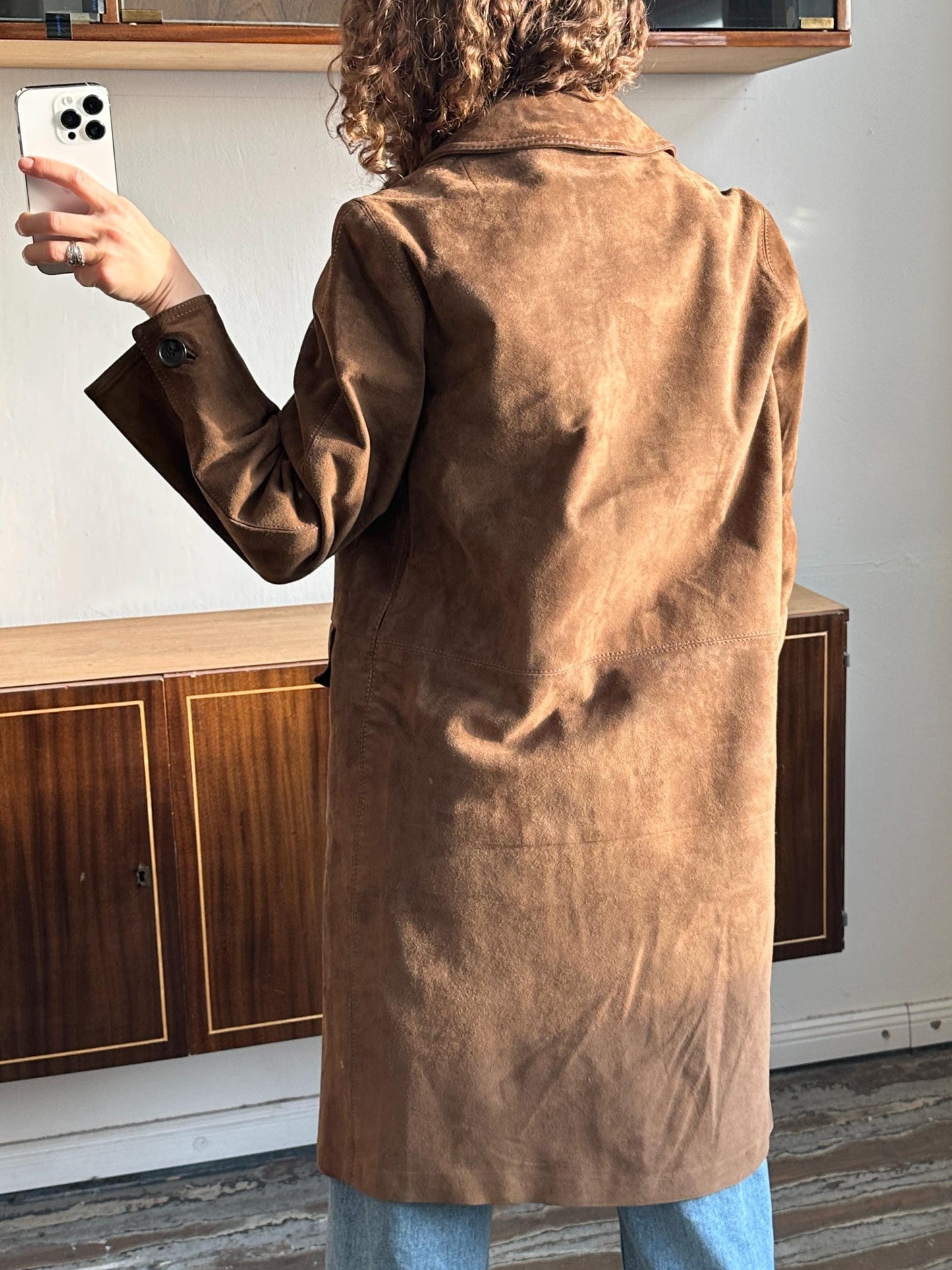 A person is taking a selfie with a brown suede coat in the background.