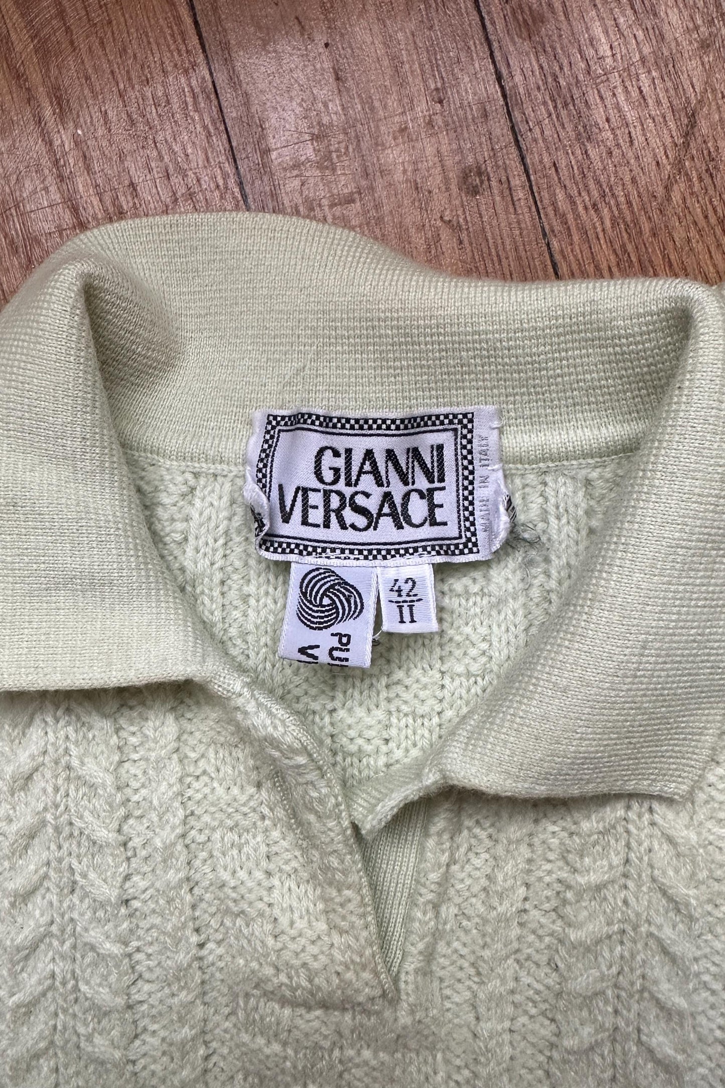 a close-up view of a cream-colored knitted sweater with a collar and a label that reads "GIANNI VERSACE".