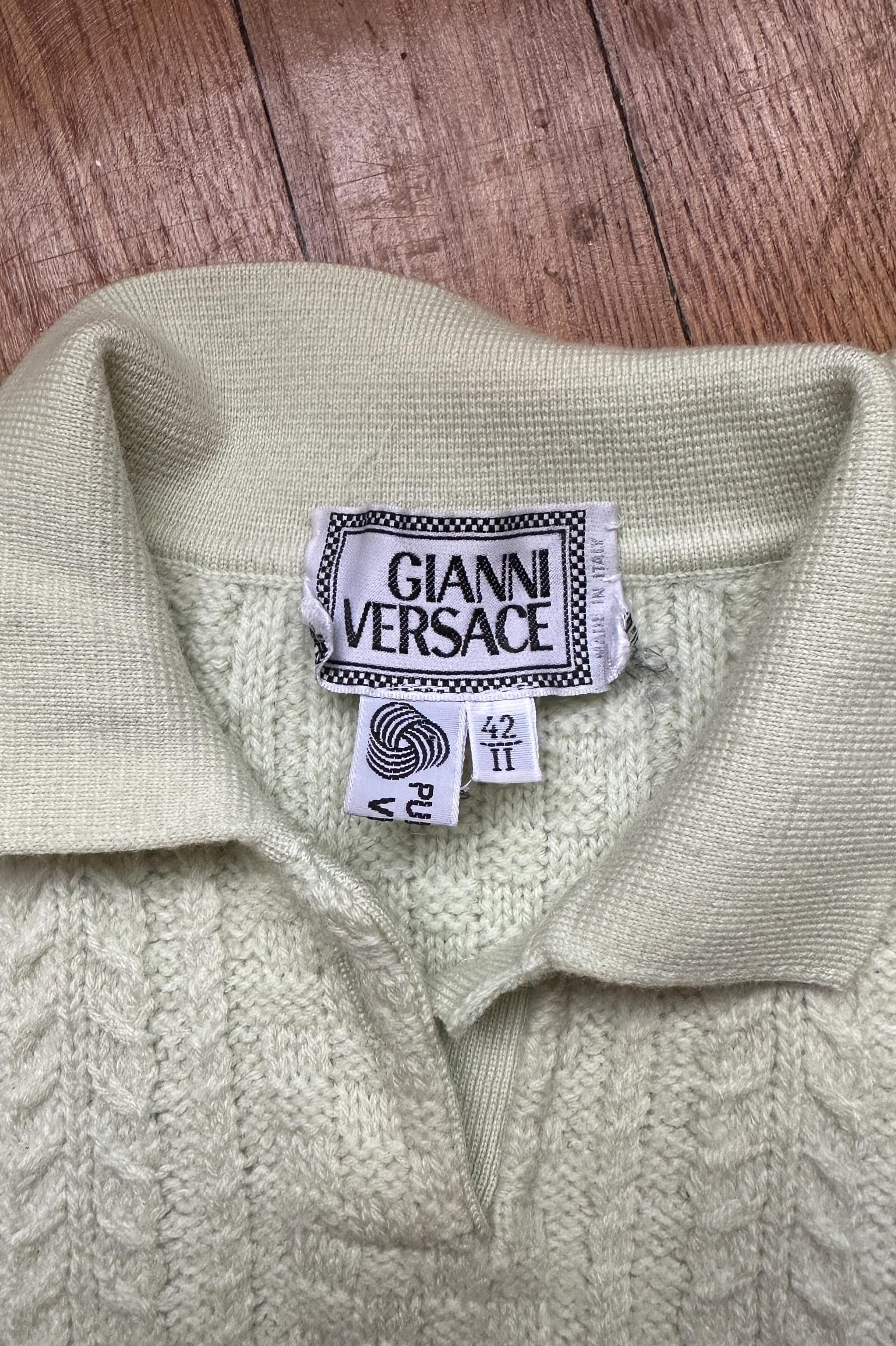 a close-up view of a cream-colored knitted sweater with a collar and a label that reads "GIANNI VERSACE".