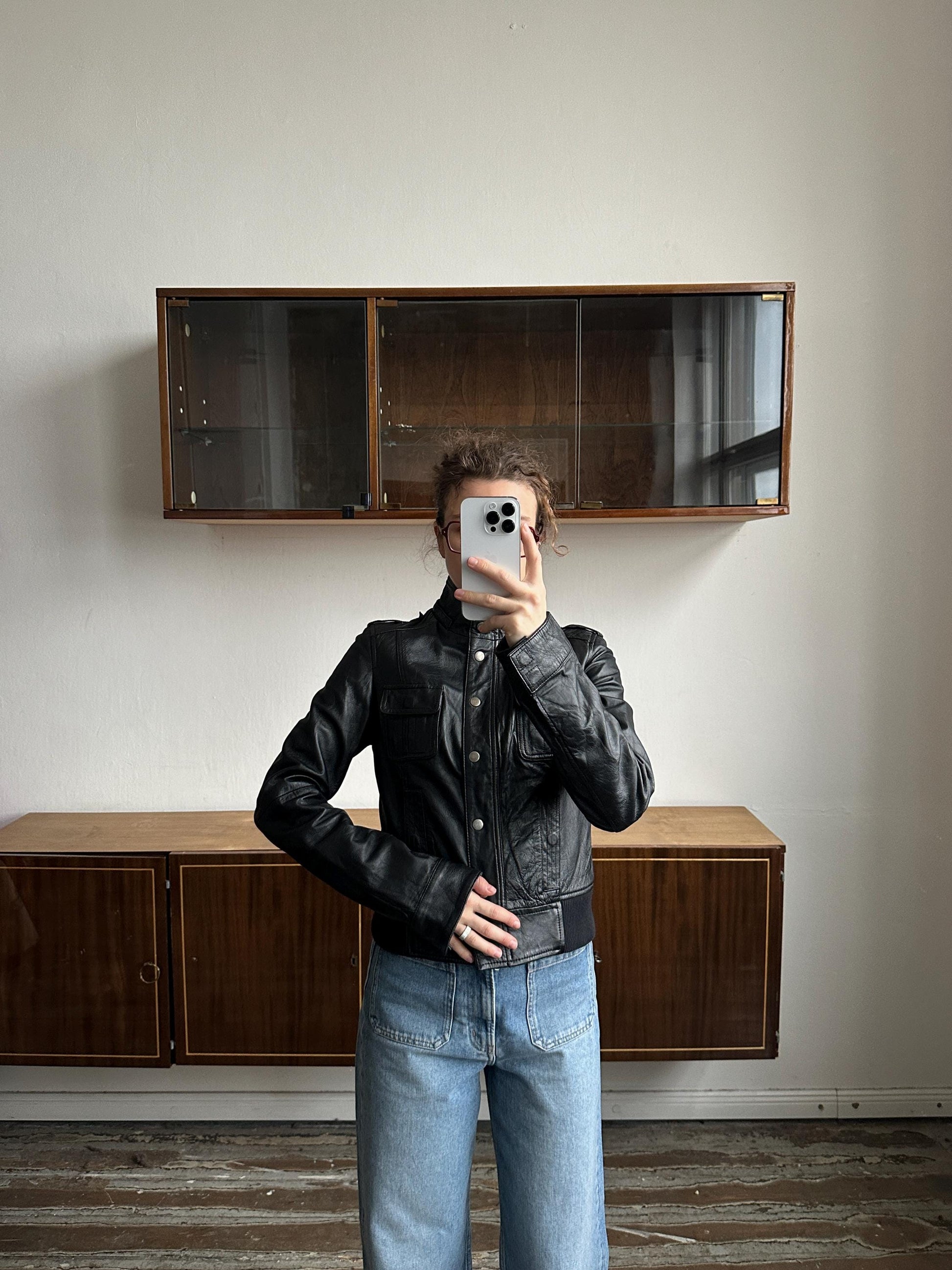 A person is taking a selfie in front of a wooden cabinet, holding a smartphone in their hand.