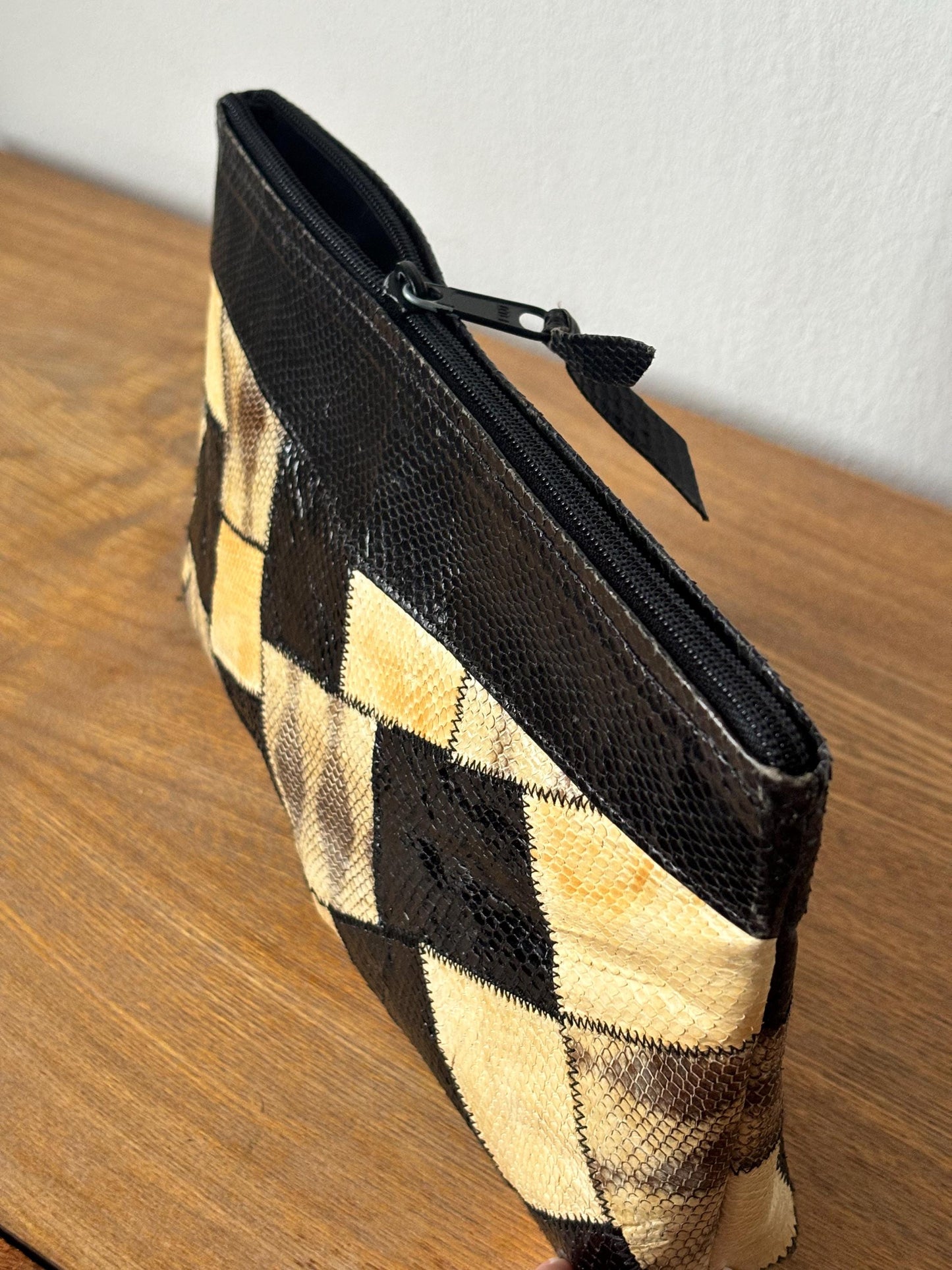 A black and tan patterned purse with a zipper closure is sitting on a wooden surface.