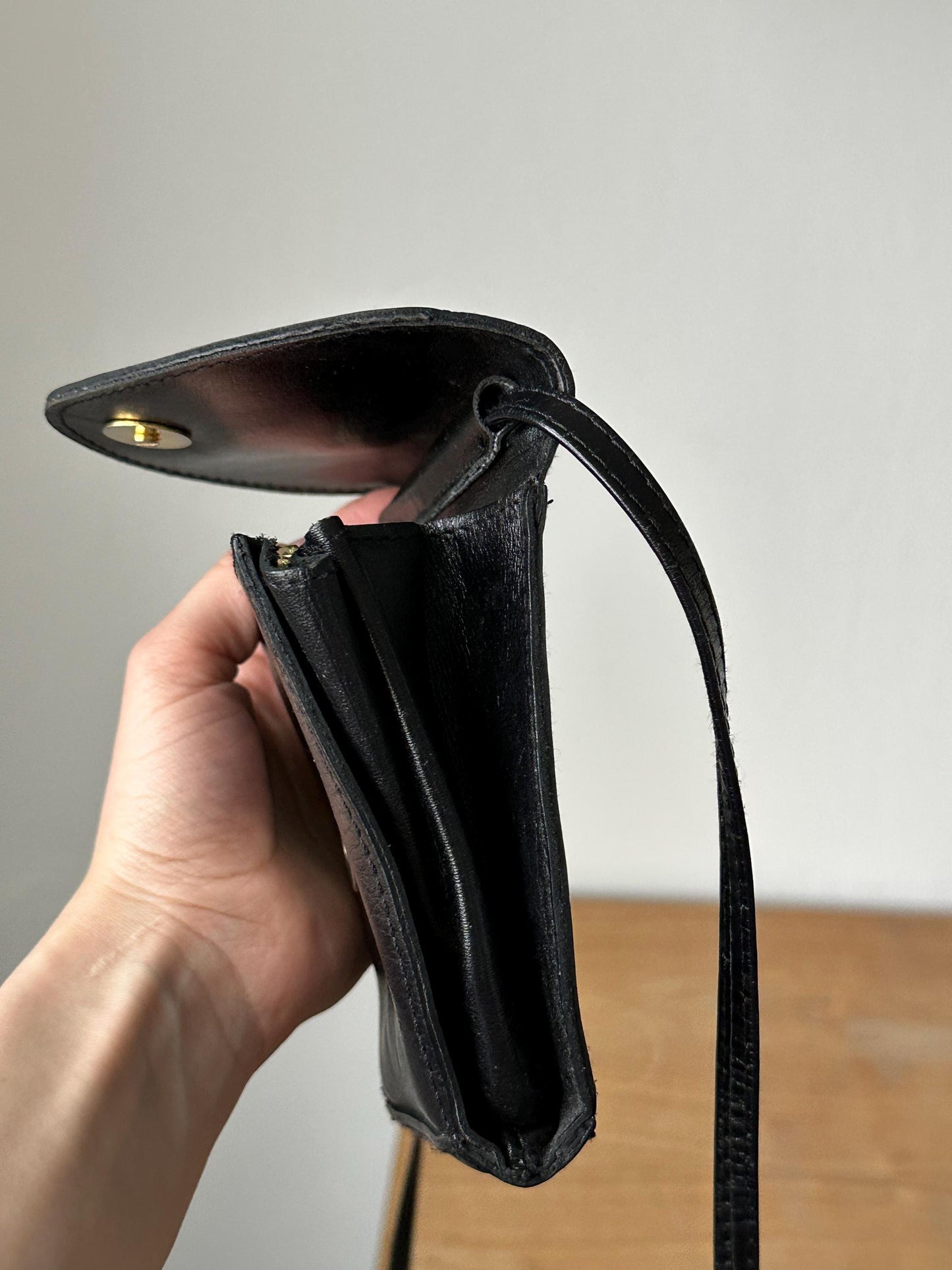 a hand holding a black purse on top of a wooden table