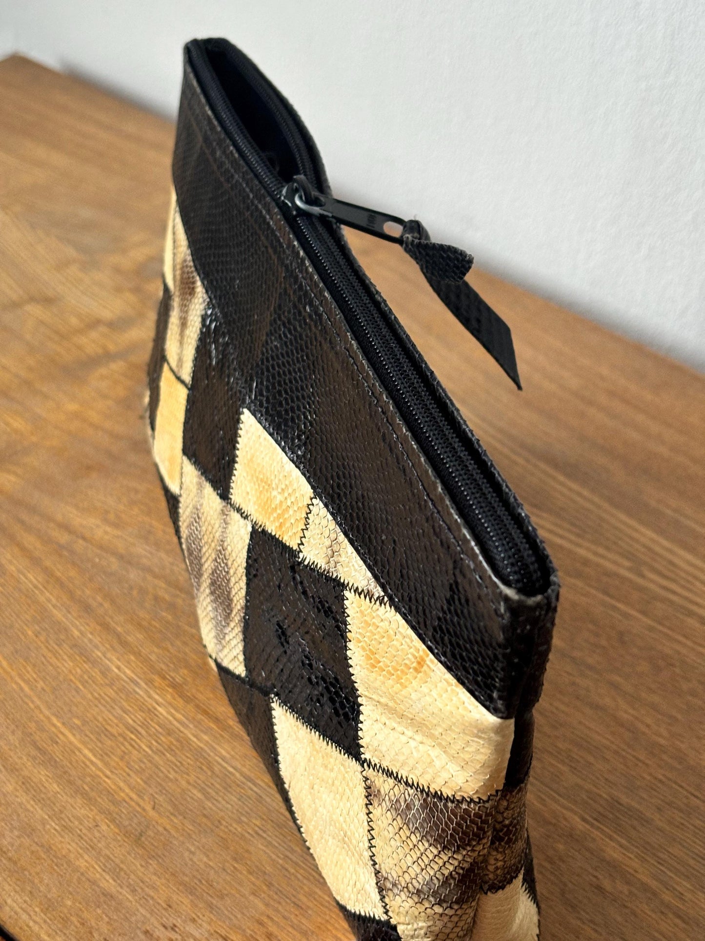 A black and tan patterned handbag with a zipper closure is sitting on a wooden surface.