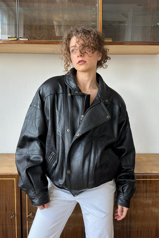 A woman wearing a black leather jacket stands in front of a glass display case.