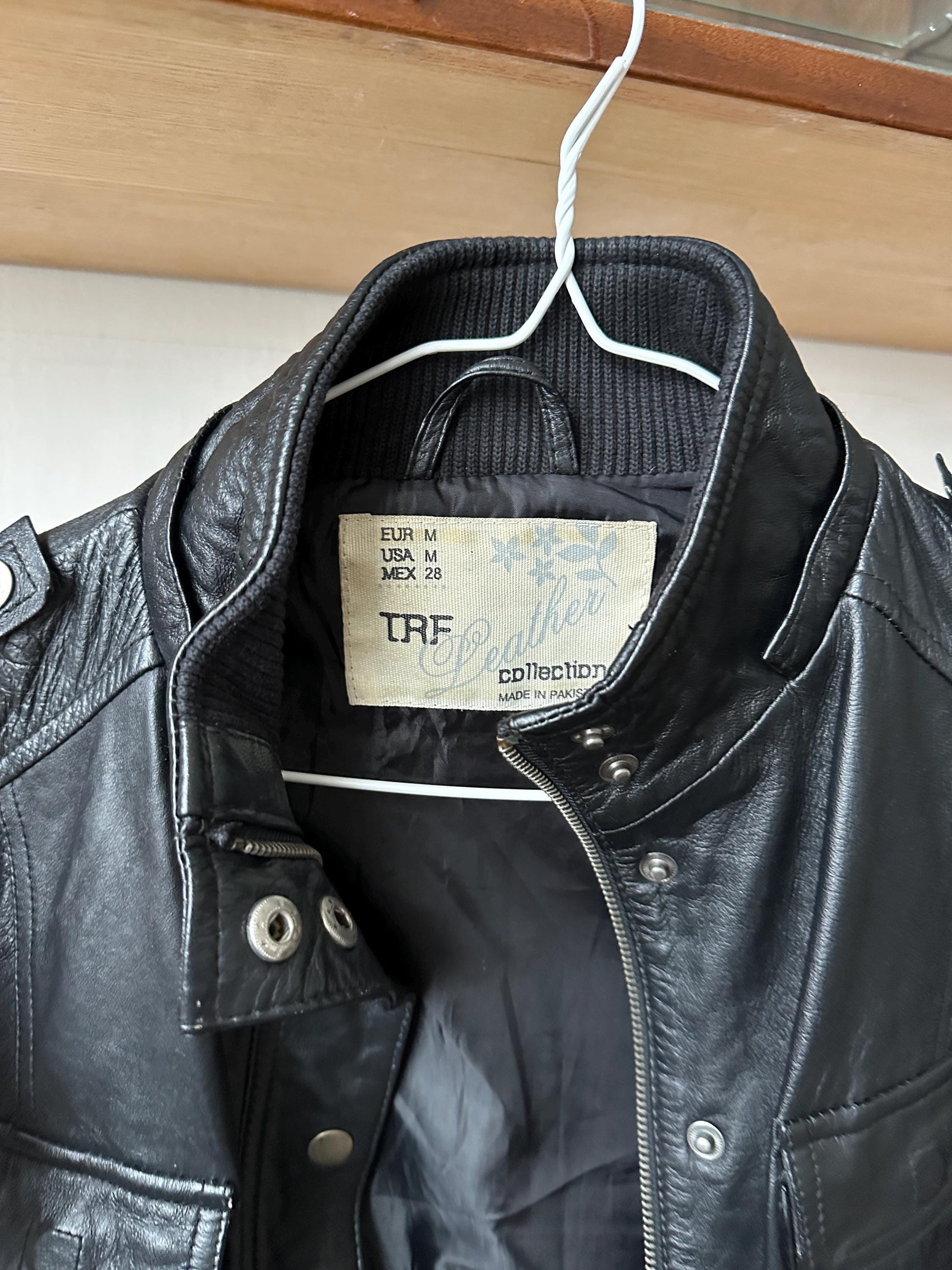 A black leather jacket hanging on a hanger, with a label attached to the collar.