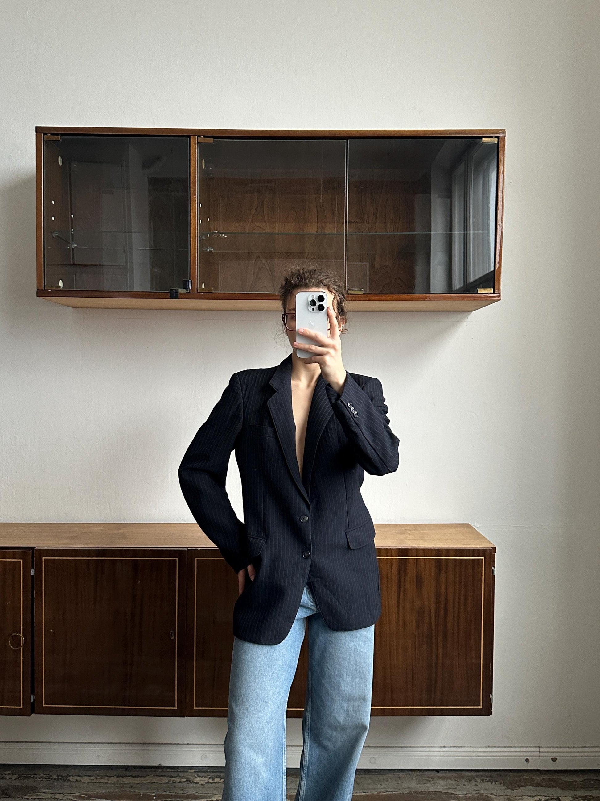 A person is taking a selfie in front of a wooden cabinet, holding a phone up to their face.