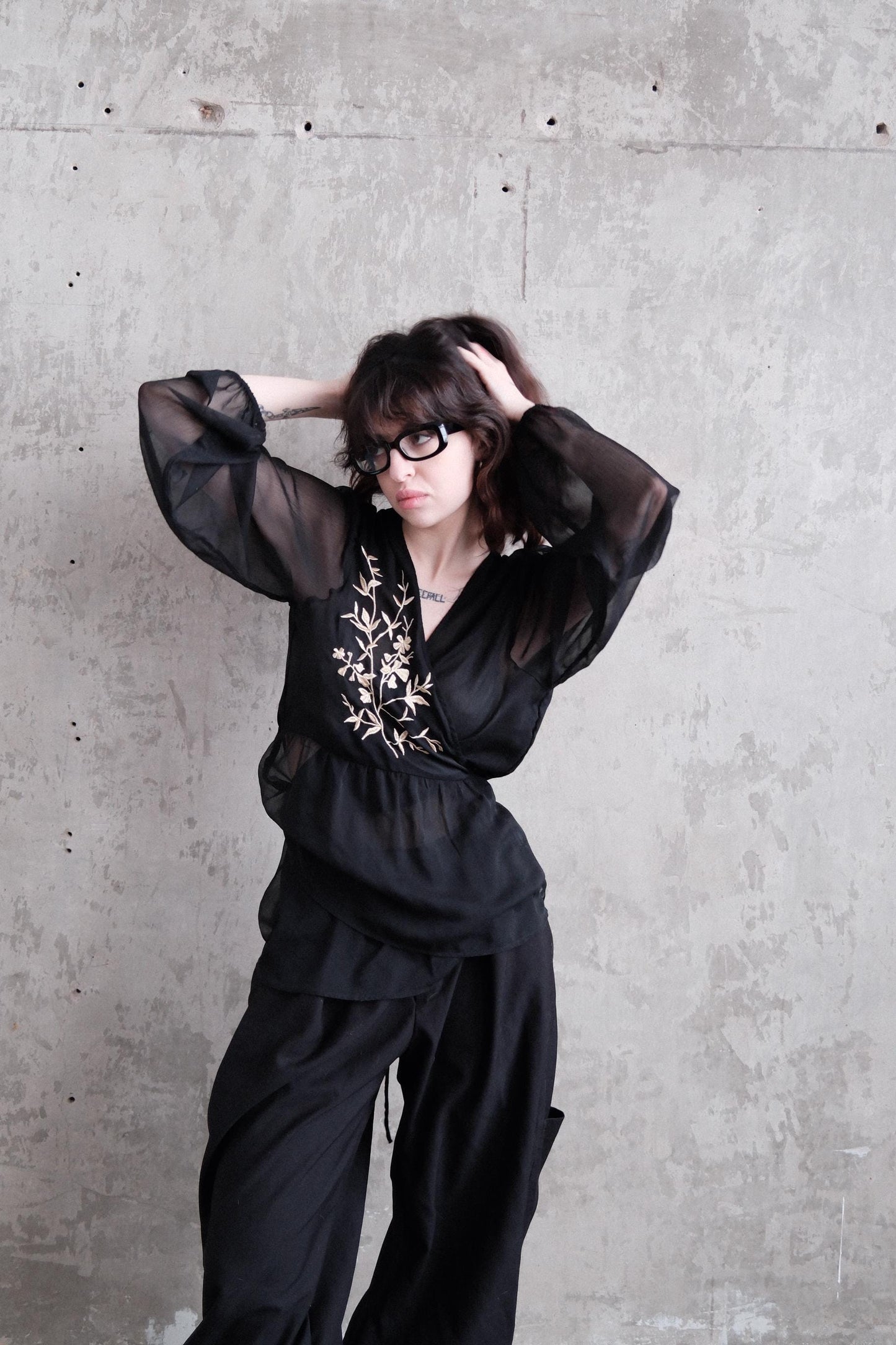 A woman in a black outfit with a floral pattern is lying on a concrete floor, her head resting on her hand.