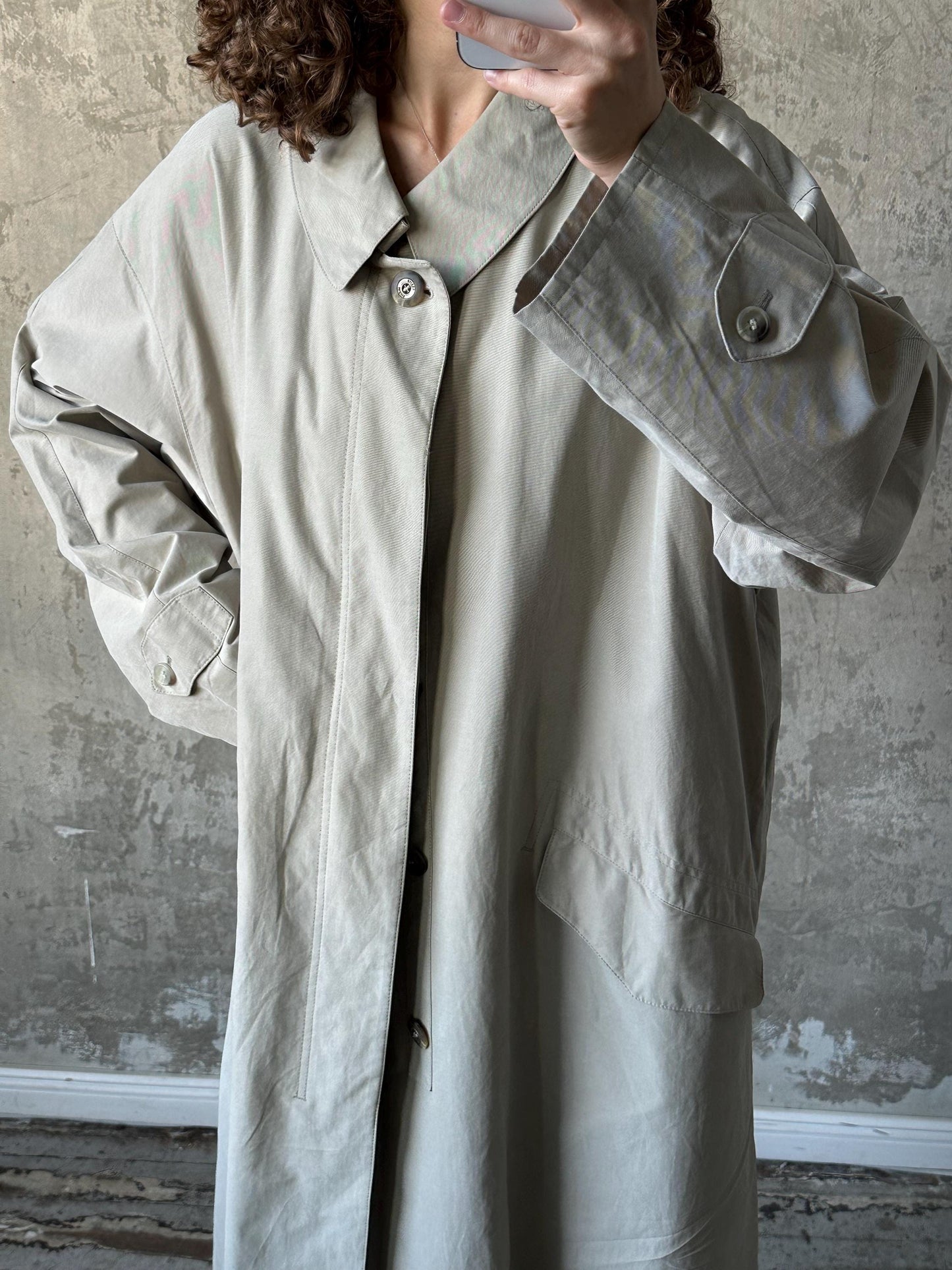 A person is taking a selfie with a camera, wearing a light-colored coat.