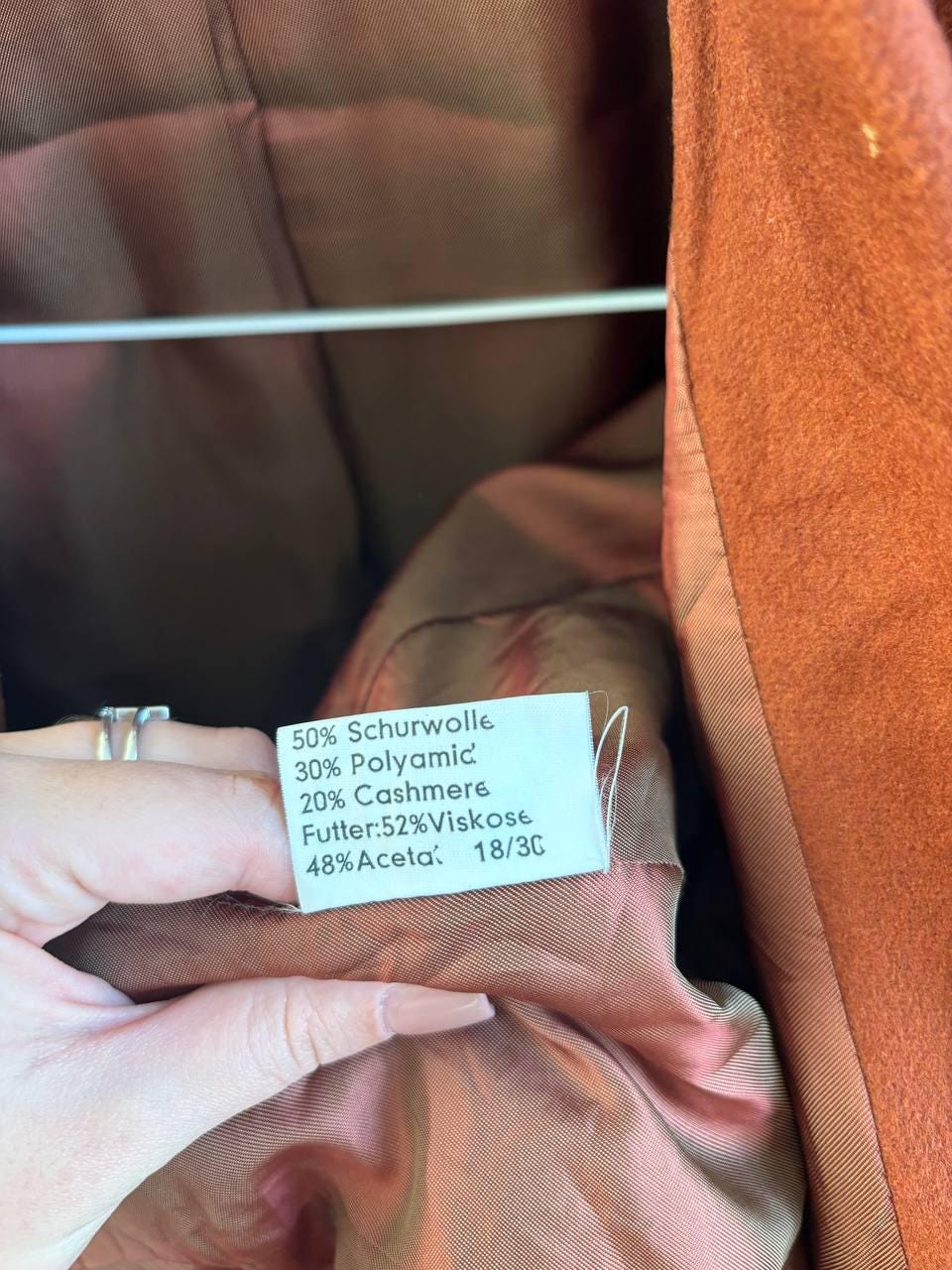 A hand holding a label with information about the fabric of a garment, specifically a wool coat.