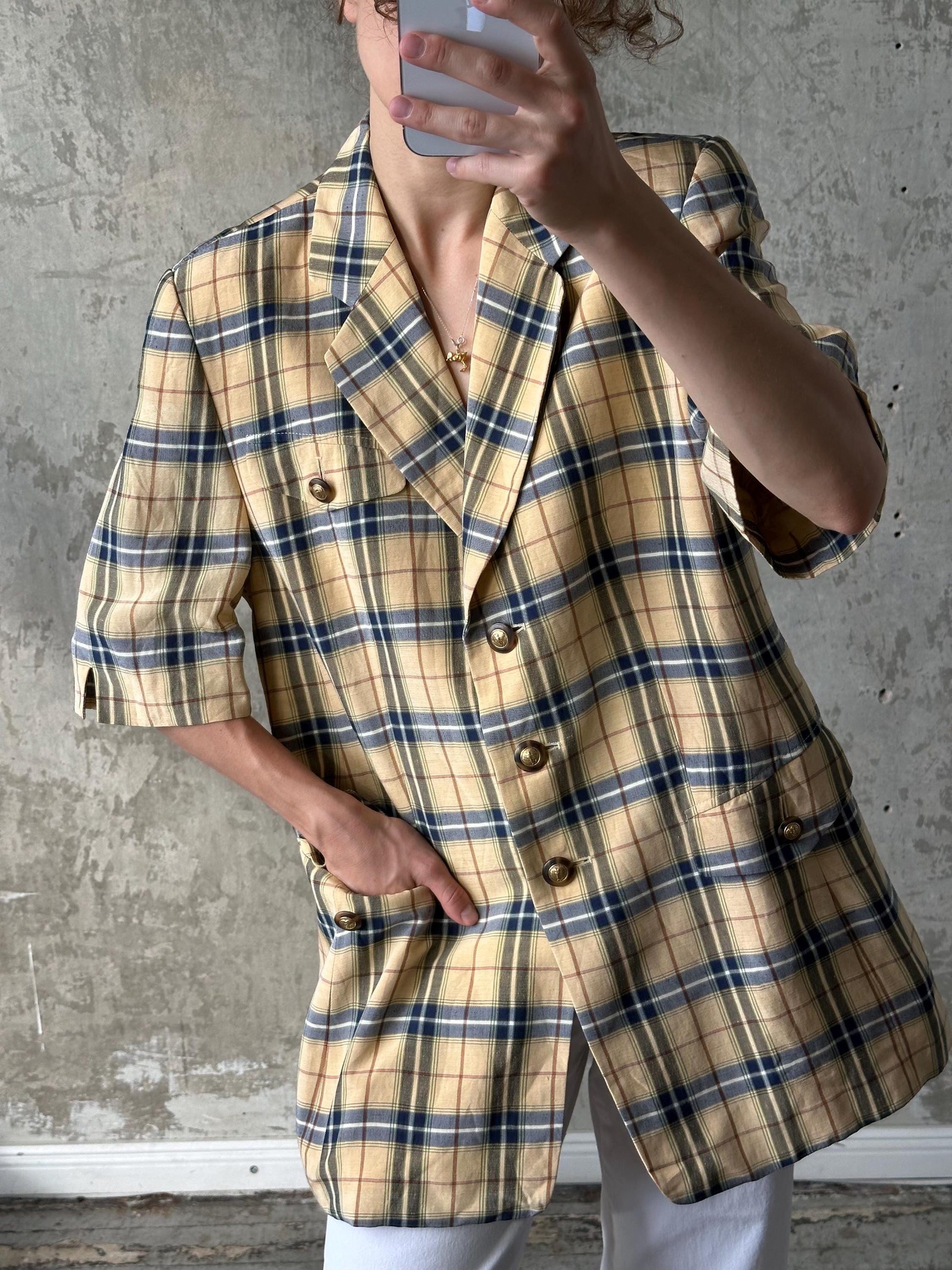 A person is taking a selfie with a plaid jacket on, holding a phone up to their face.