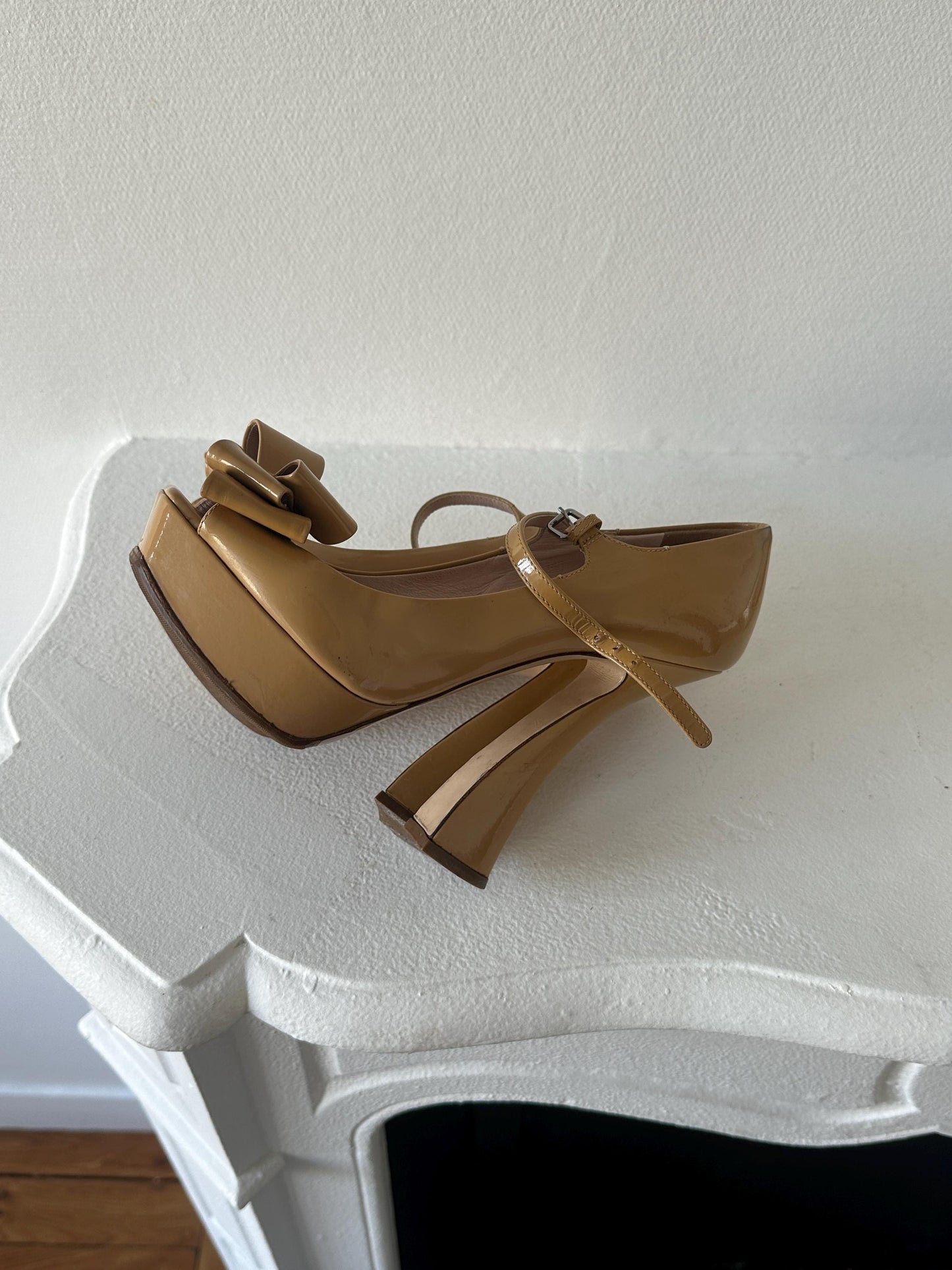 A tan high-heeled shoe with a bow detail is displayed on a white surface.