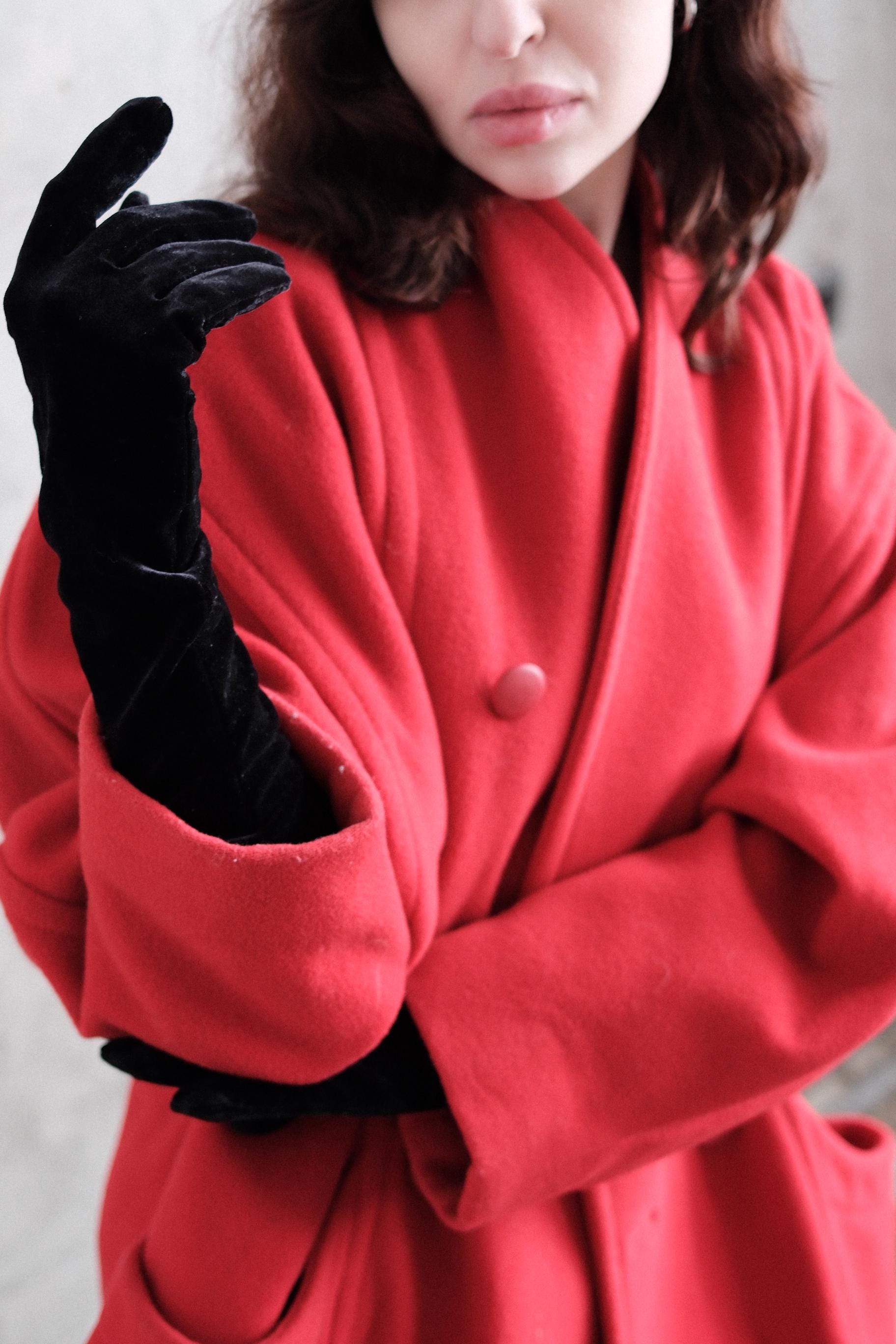A close-up of a person wearing a red coat and black gloves, with their hand extended.