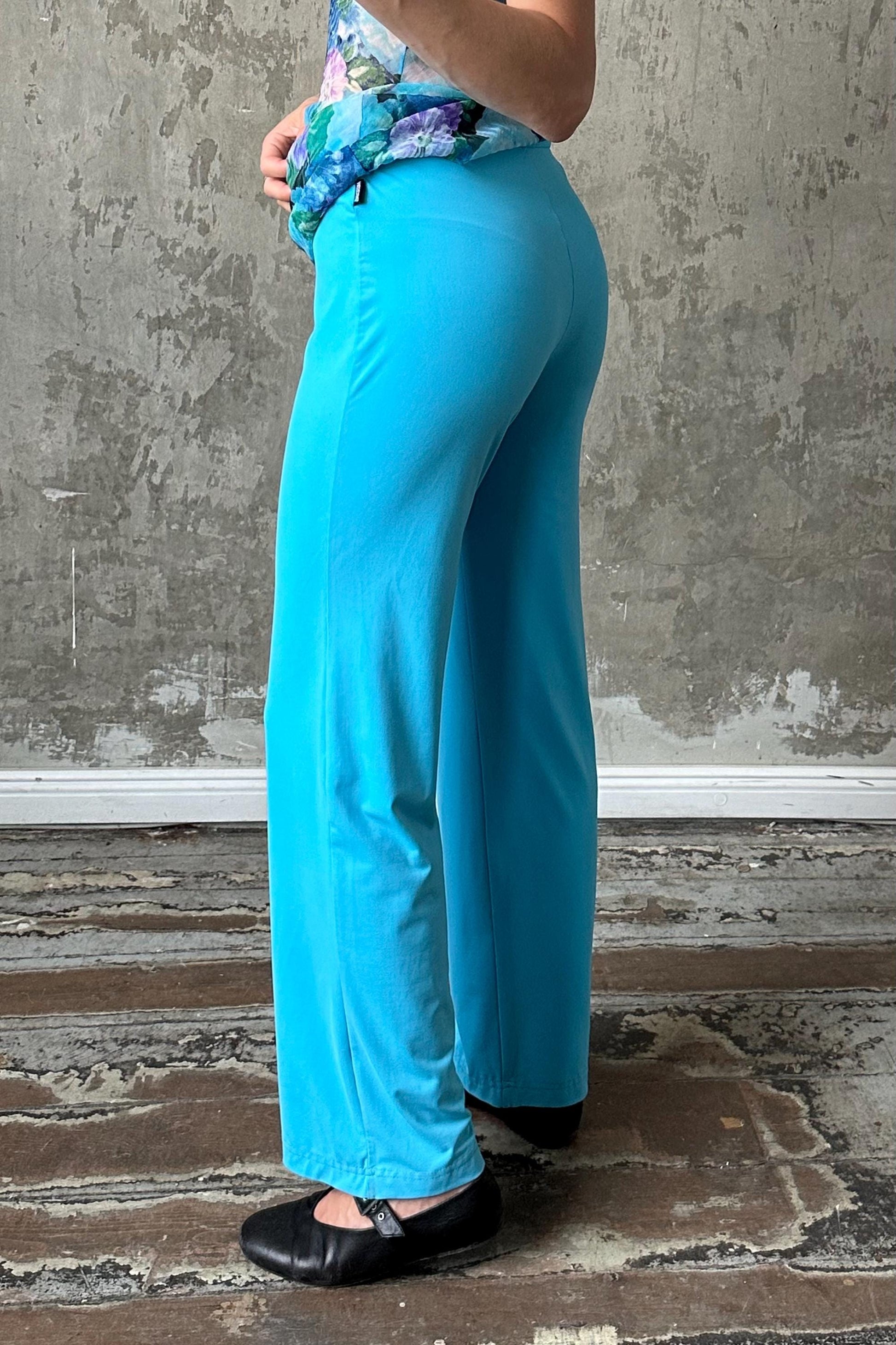 A person wearing a blue floral top and wide-leg pants stands in front of a concrete wall.