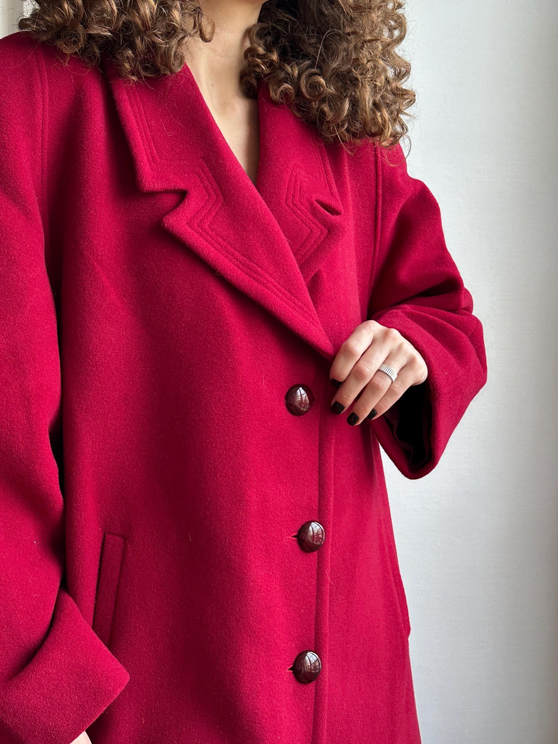 A person wearing a red coat with their hand on the buttons, lying on a white surface.