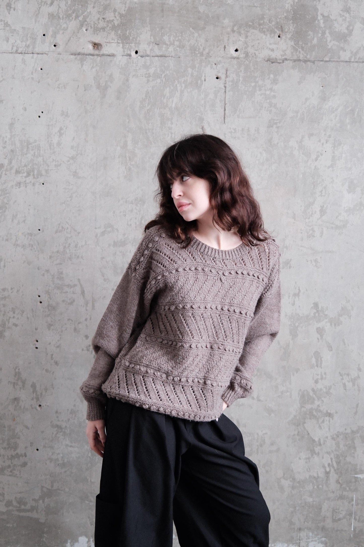 A woman with long brown hair is lying on a concrete floor, wearing a gray sweater.