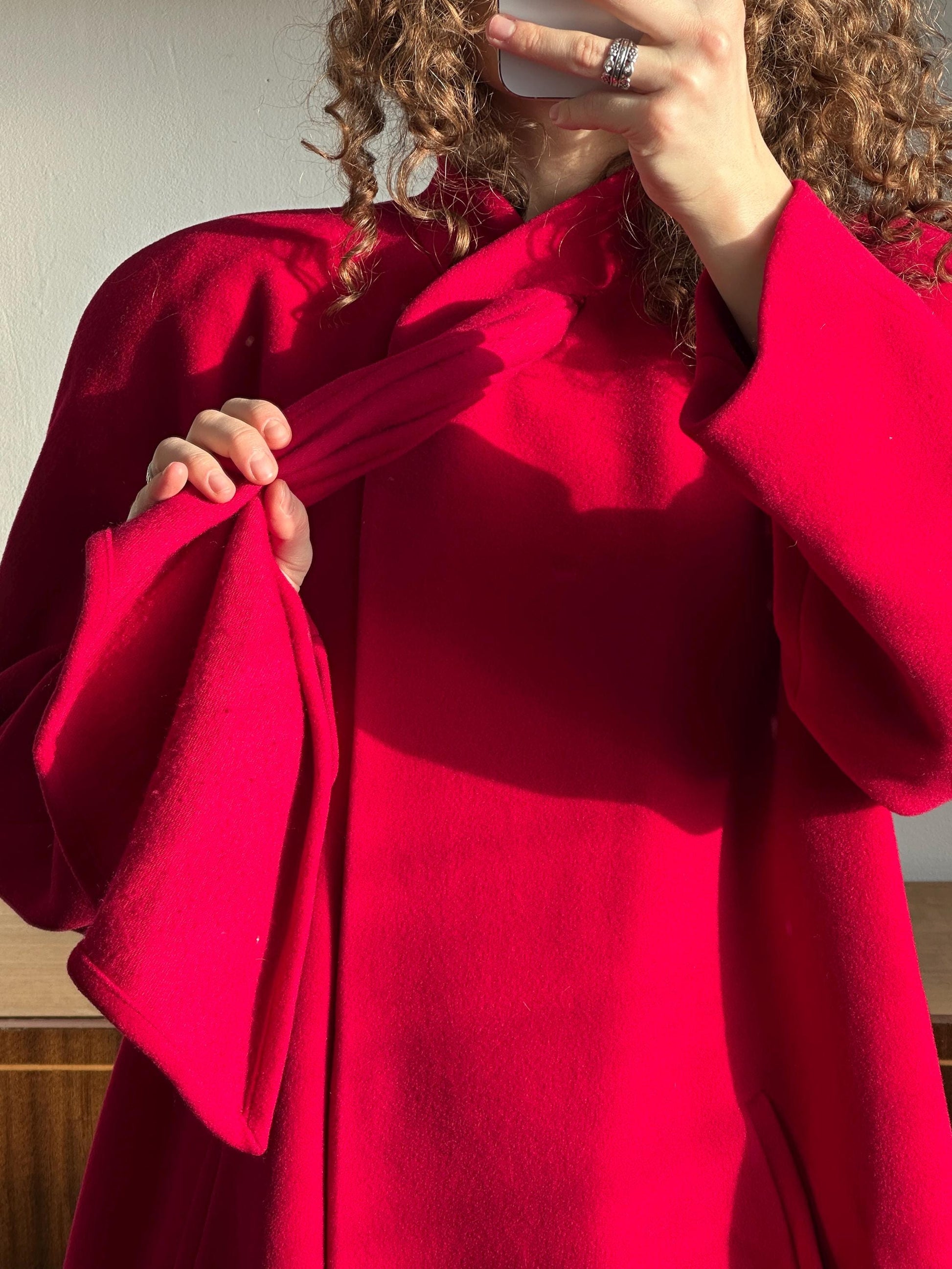 A person wearing a red coat is taking a selfie, with their curly hair visible in the mirror.