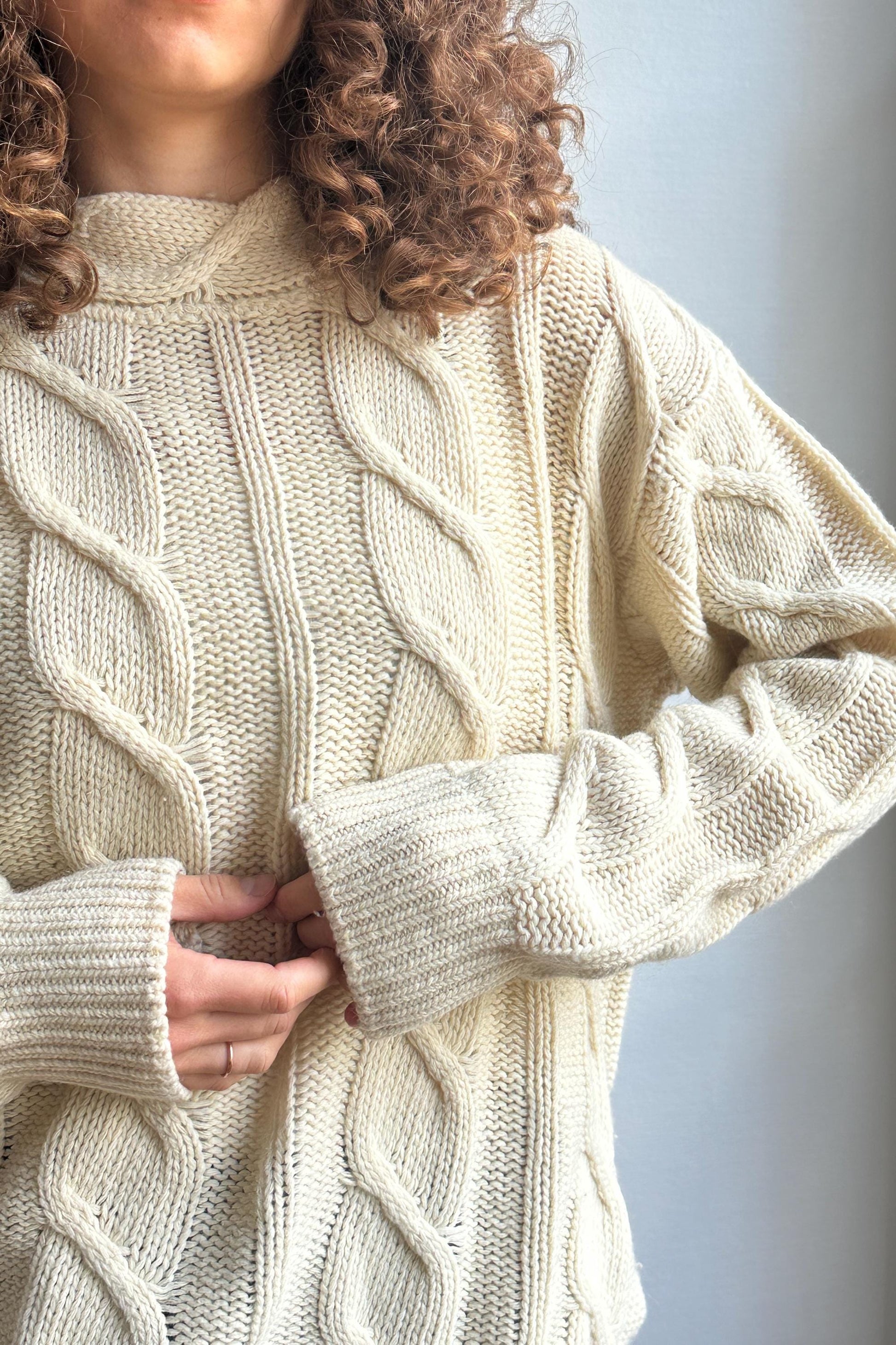 A close-up of a person wearing a cream-colored knitted sweater with a high collar and long sleeves.
