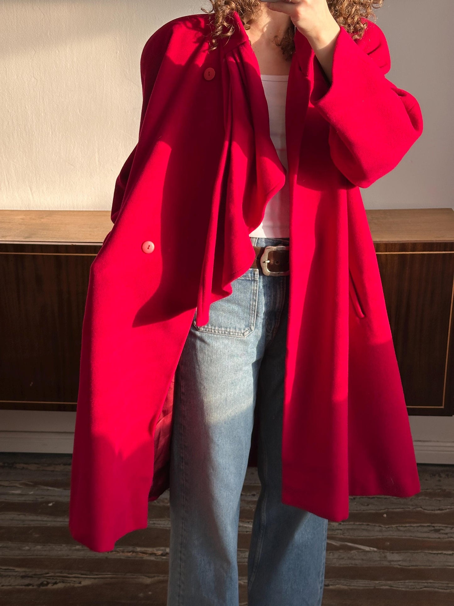 A person wearing a red coat and jeans is standing in front of a wooden door.