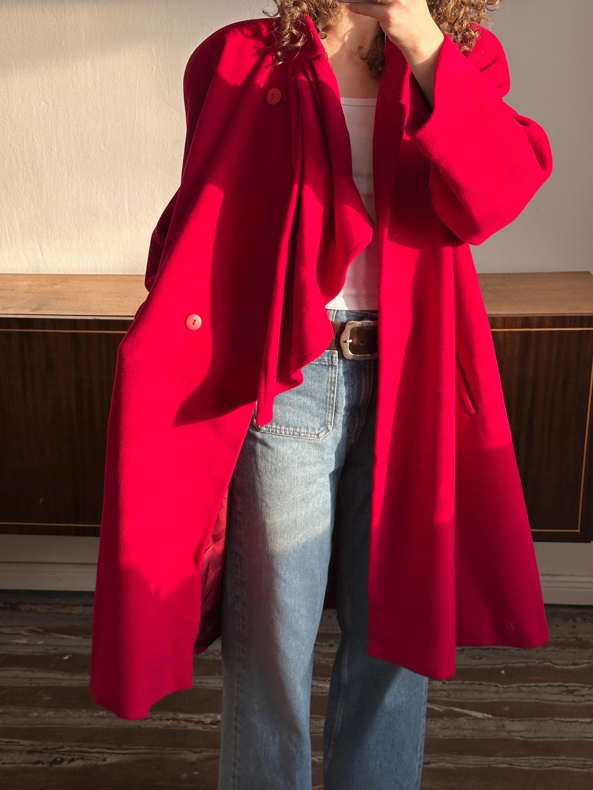A person wearing a red coat and jeans is standing in front of a wooden door.