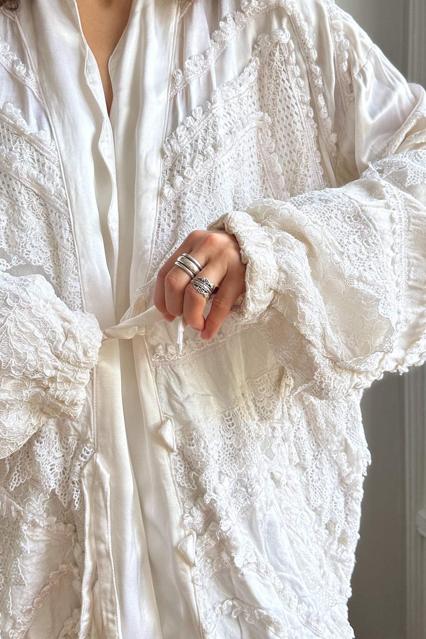 A close-up of a person wearing a white lace robe with a lace collar, and a ring on their finger.