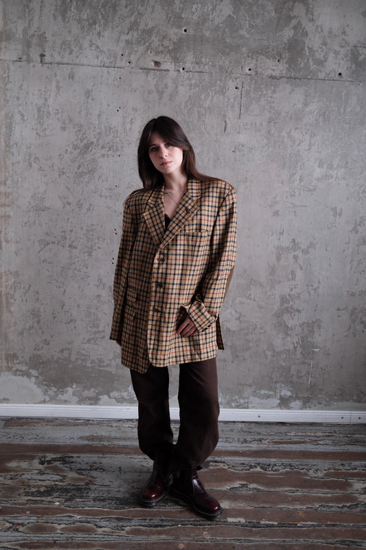 A woman wearing a plaid jacket stands in a room with a concrete wall.
