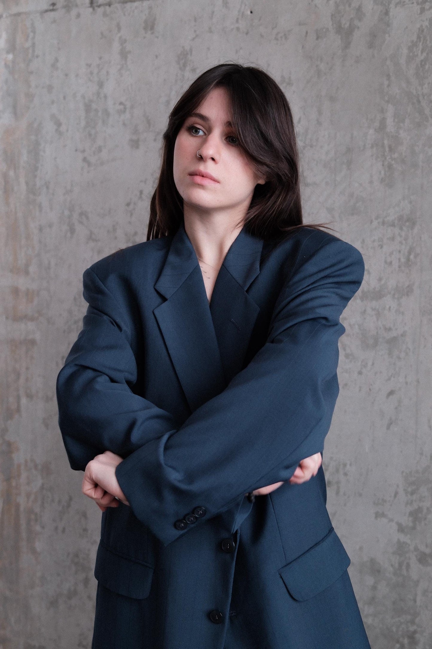 A woman in a dark blue suit stands with her arms crossed, looking directly at the camera.