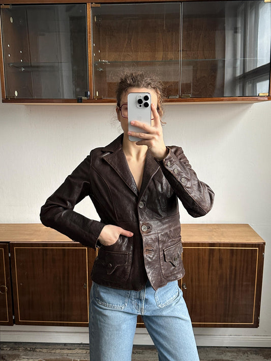 A person is taking a selfie with a smartphone, wearing a brown leather jacket and blue jeans.