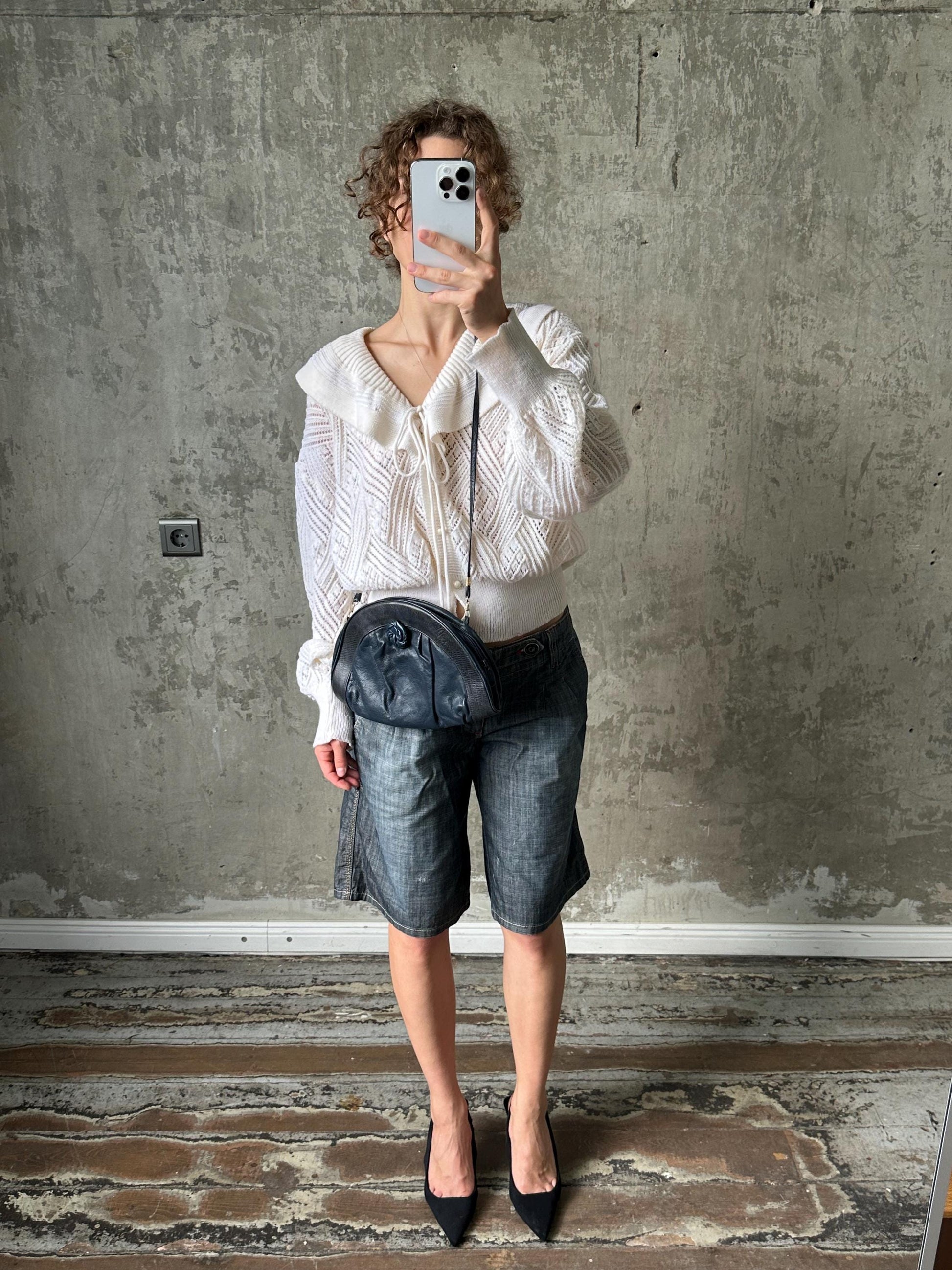 A person is taking a selfie with a white phone, standing in front of a concrete wall.