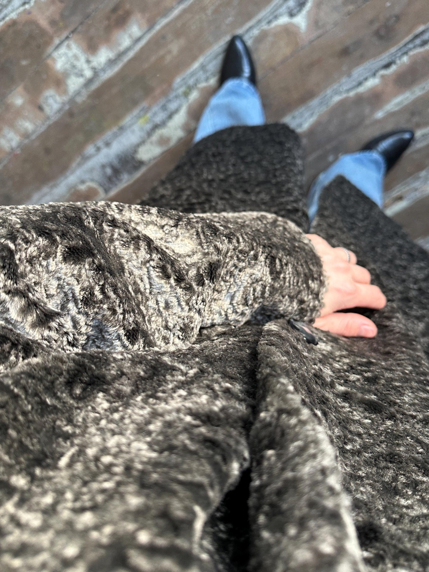 A close-up view of a person's hand resting on a furry coat, with a blurred background of a wooden floor.