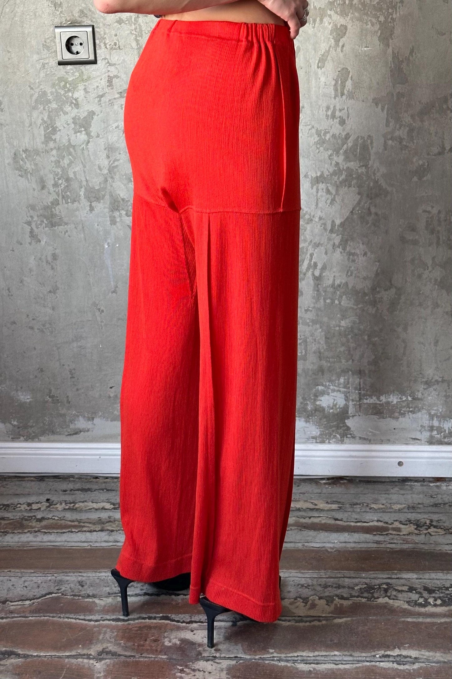 a person wearing a bright red pair of wide-leg pants standing against a concrete wall.