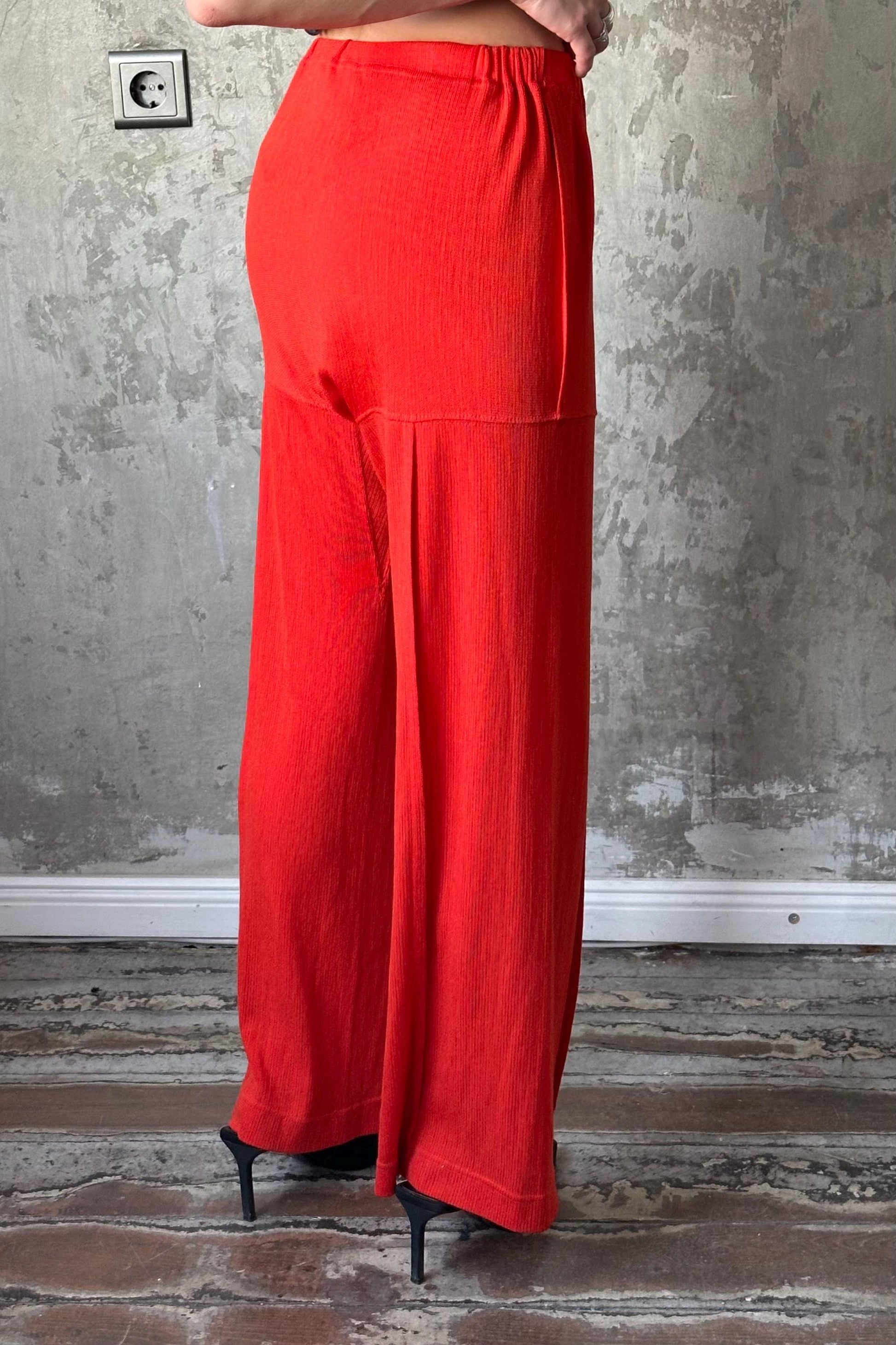 a person wearing a bright red pair of wide-leg pants standing against a concrete wall.