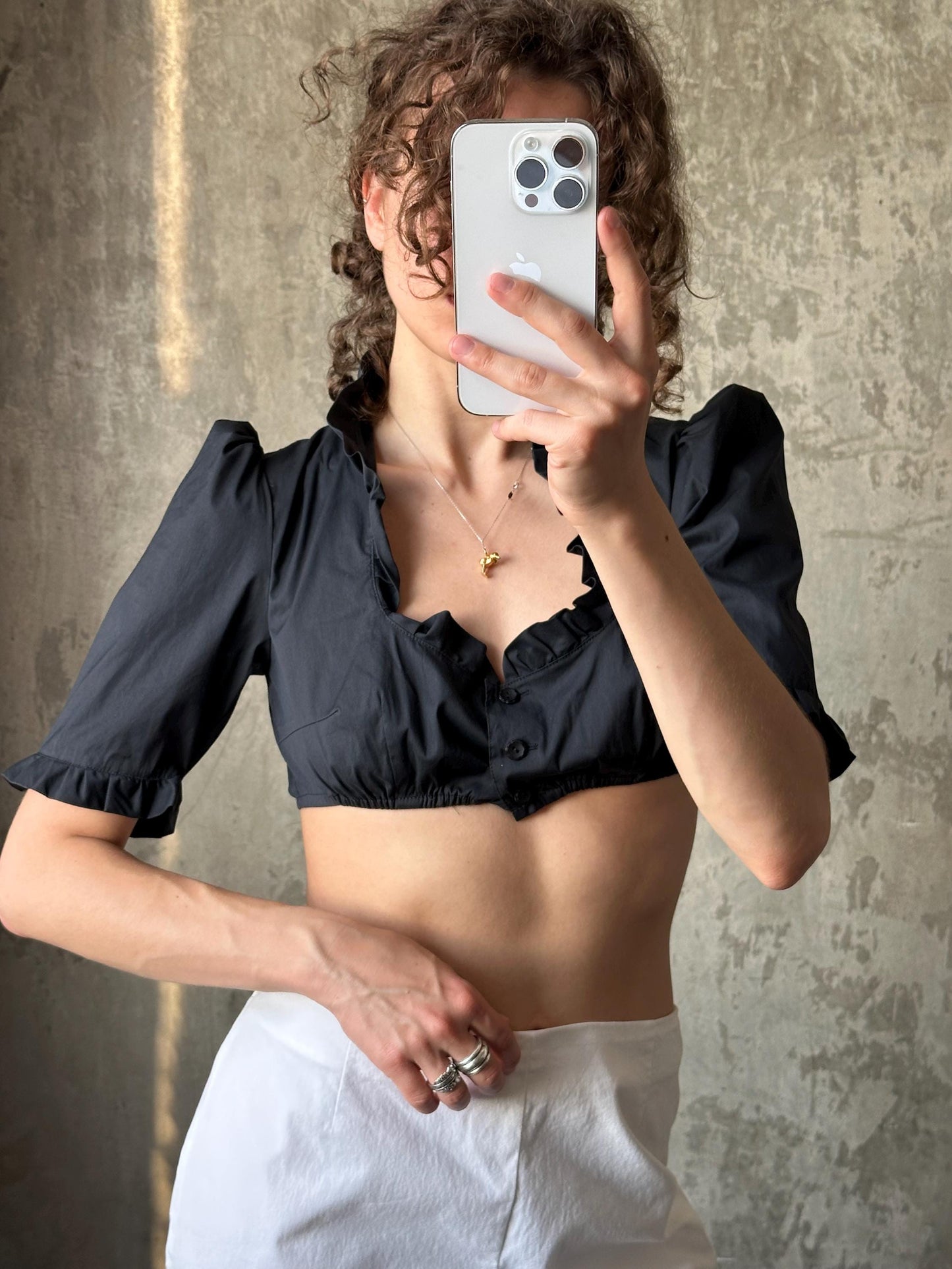 A woman is taking a selfie with her iPhone, holding it up to her face against a concrete wall.