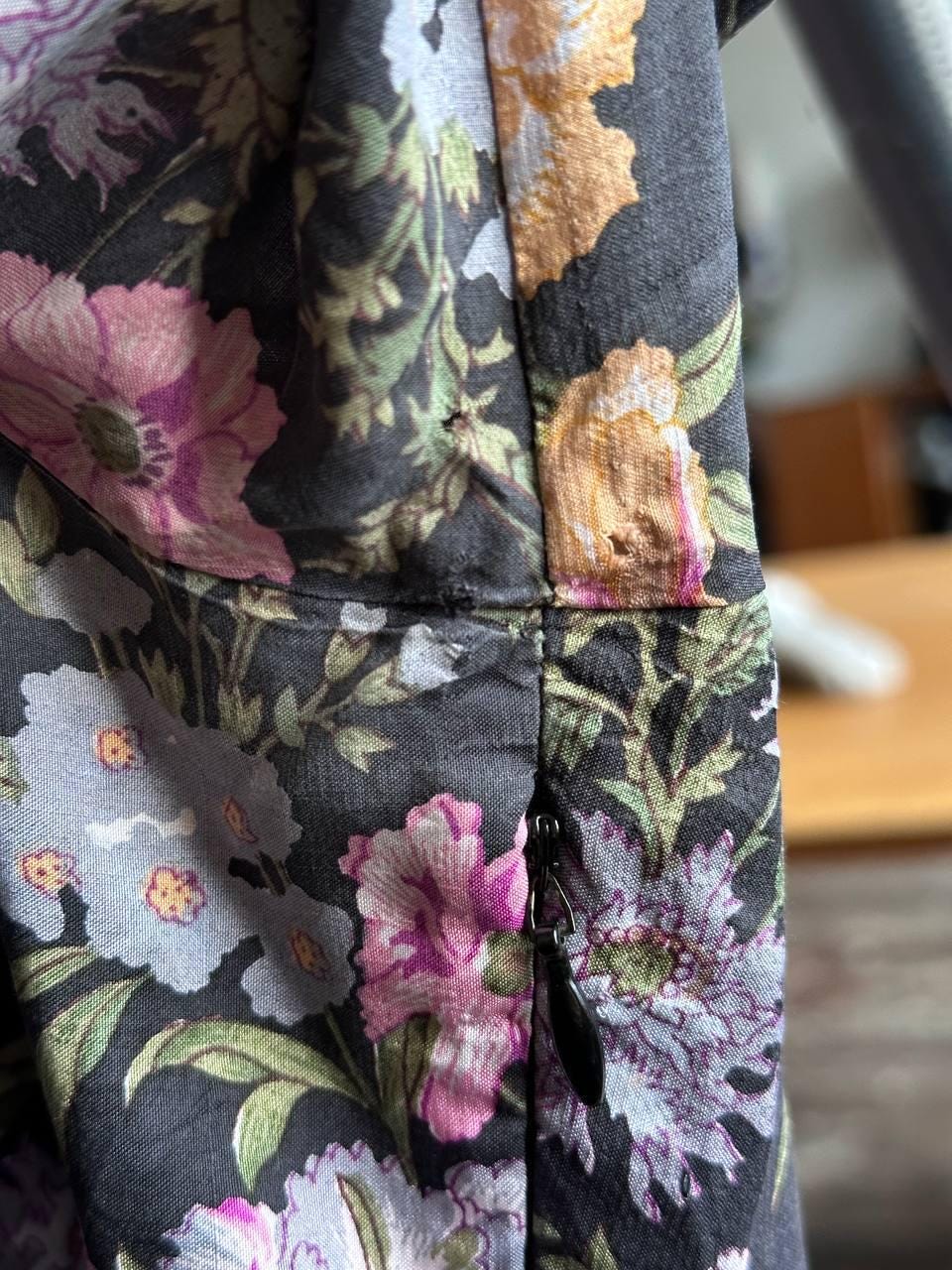 a close-up view of a floral print fabric, featuring a variety of colorful flowers and leaves. The fabric appears to be a dark-colored material with a floral pattern.