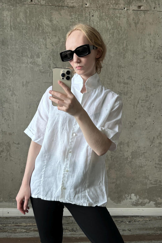 A woman wearing a white shirt and sunglasses is taking a selfie with a smartphone.