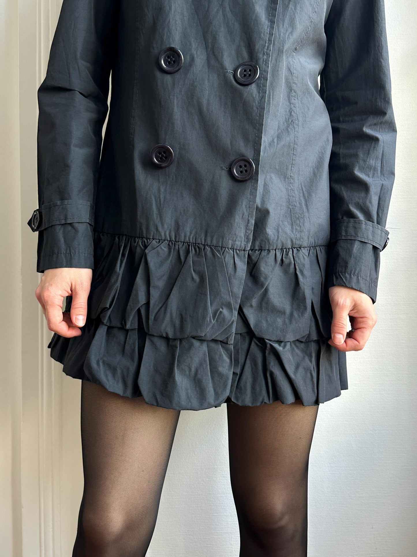 A person wearing a black coat with ruffled details and black stockings is shown in a relaxed pose.