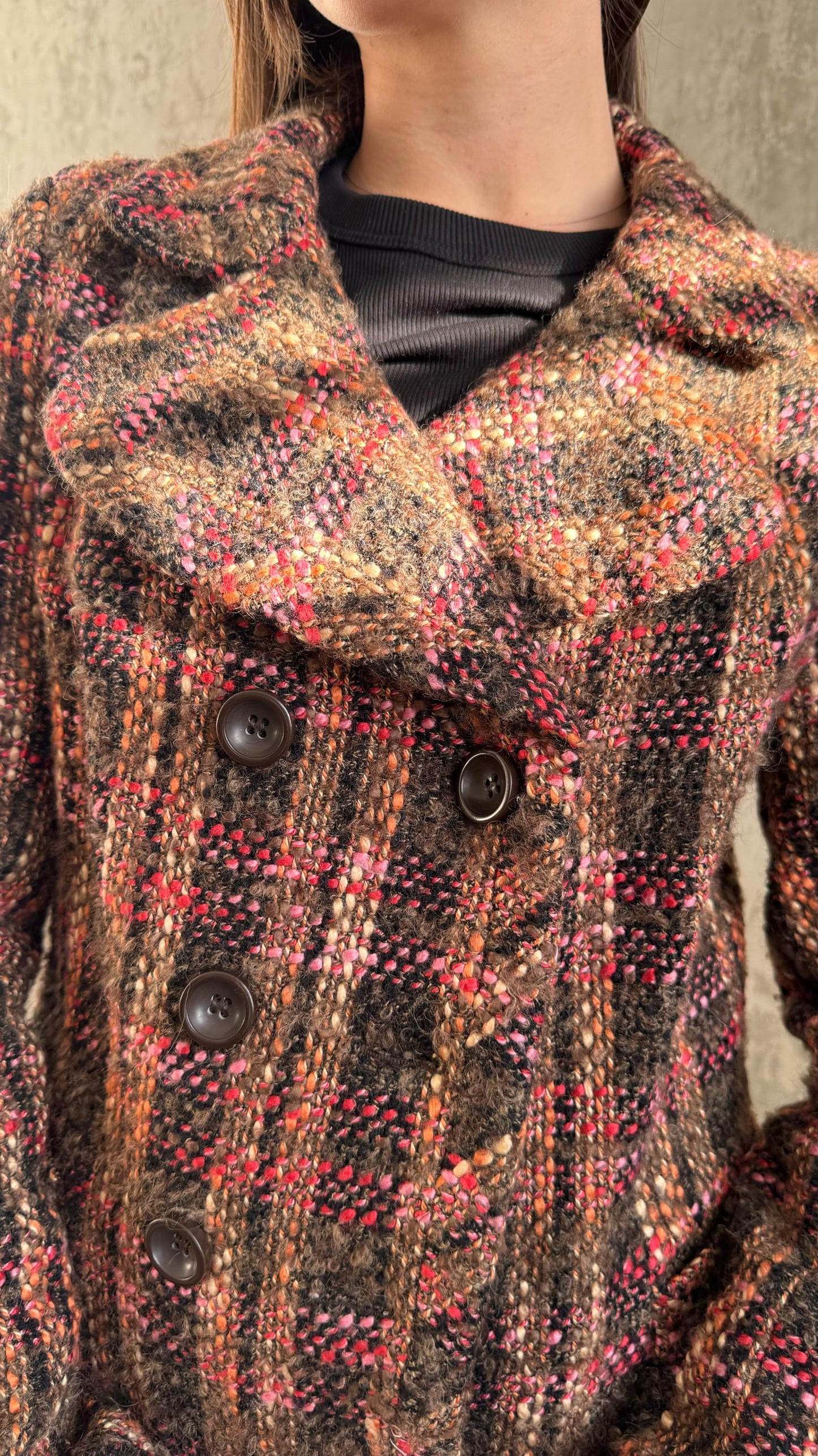 A close-up image of a woman wearing a brown plaid coat with three buttons.