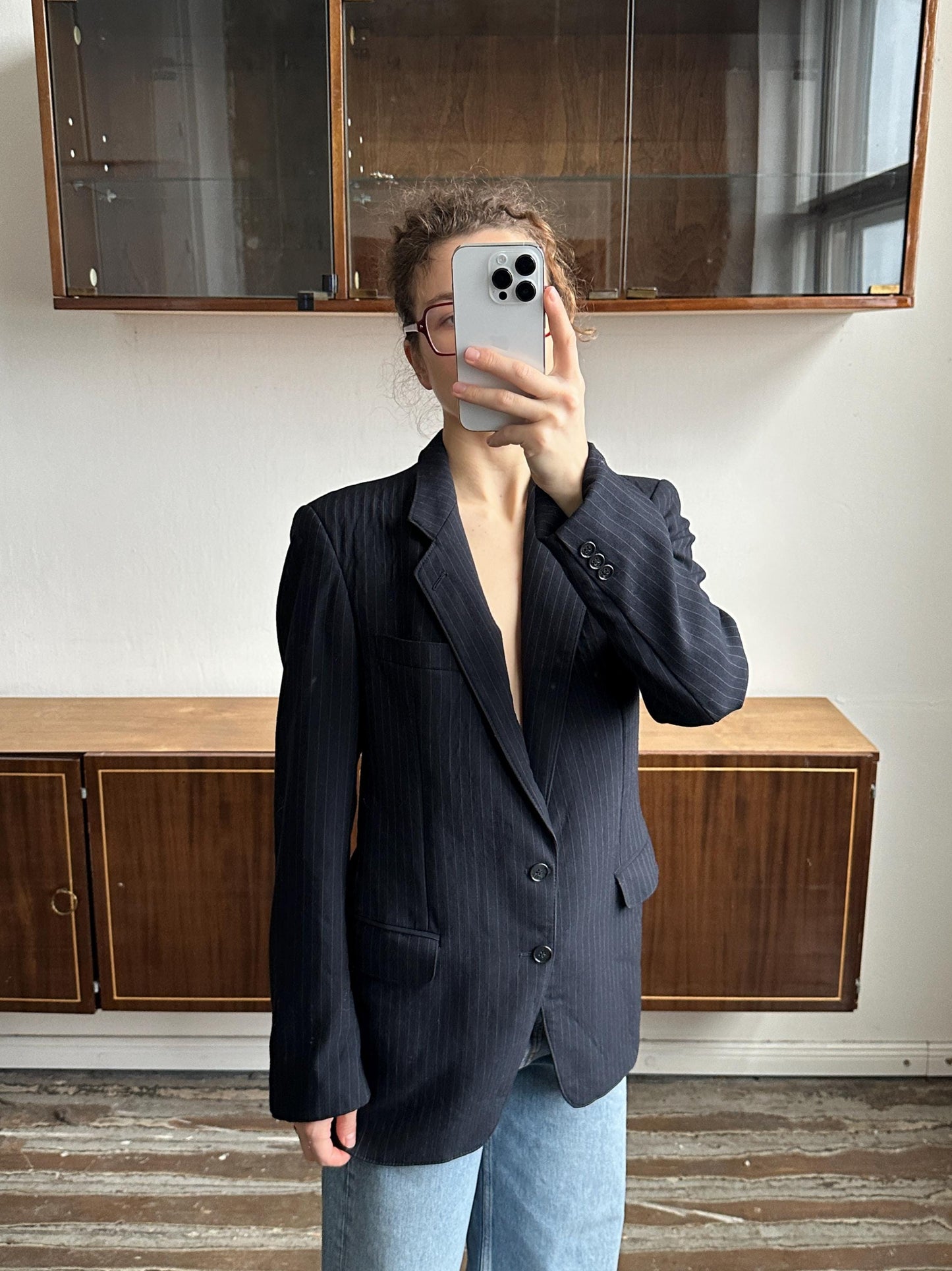 A person is taking a selfie with a smartphone, holding the phone up to their face in front of a wooden cabinet.