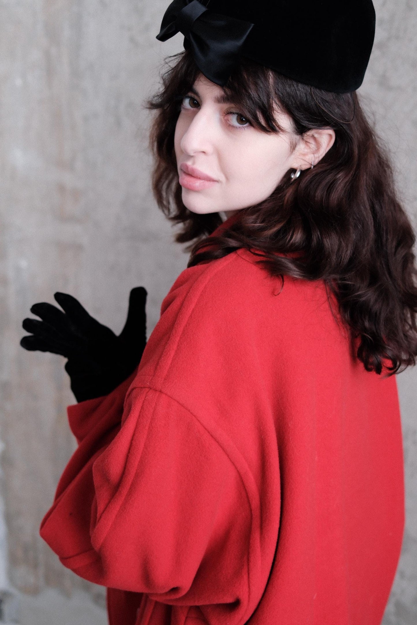 A woman wearing a red coat and black gloves is lying on her stomach, with her head tilted back and her eyes looking up.